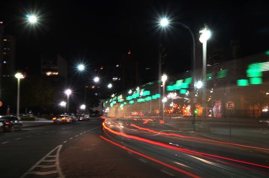 Dynamic cityscape featuring blurred traffic lights and illuminated buildings at night, showcasing urban energy.
