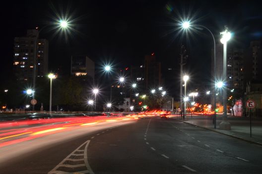 Urban night scene with vehicle light trails under streetlights.