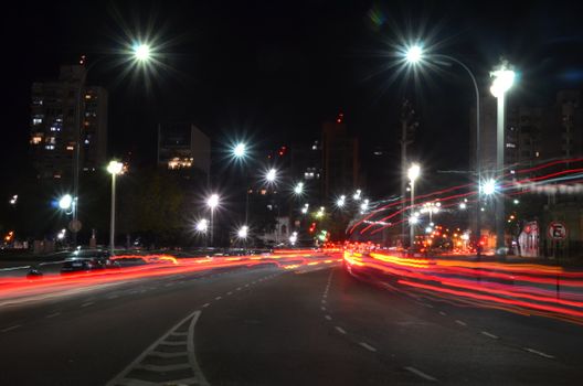 A vibrant urban scene at night featuring glowing car light trails and bright streetlights.