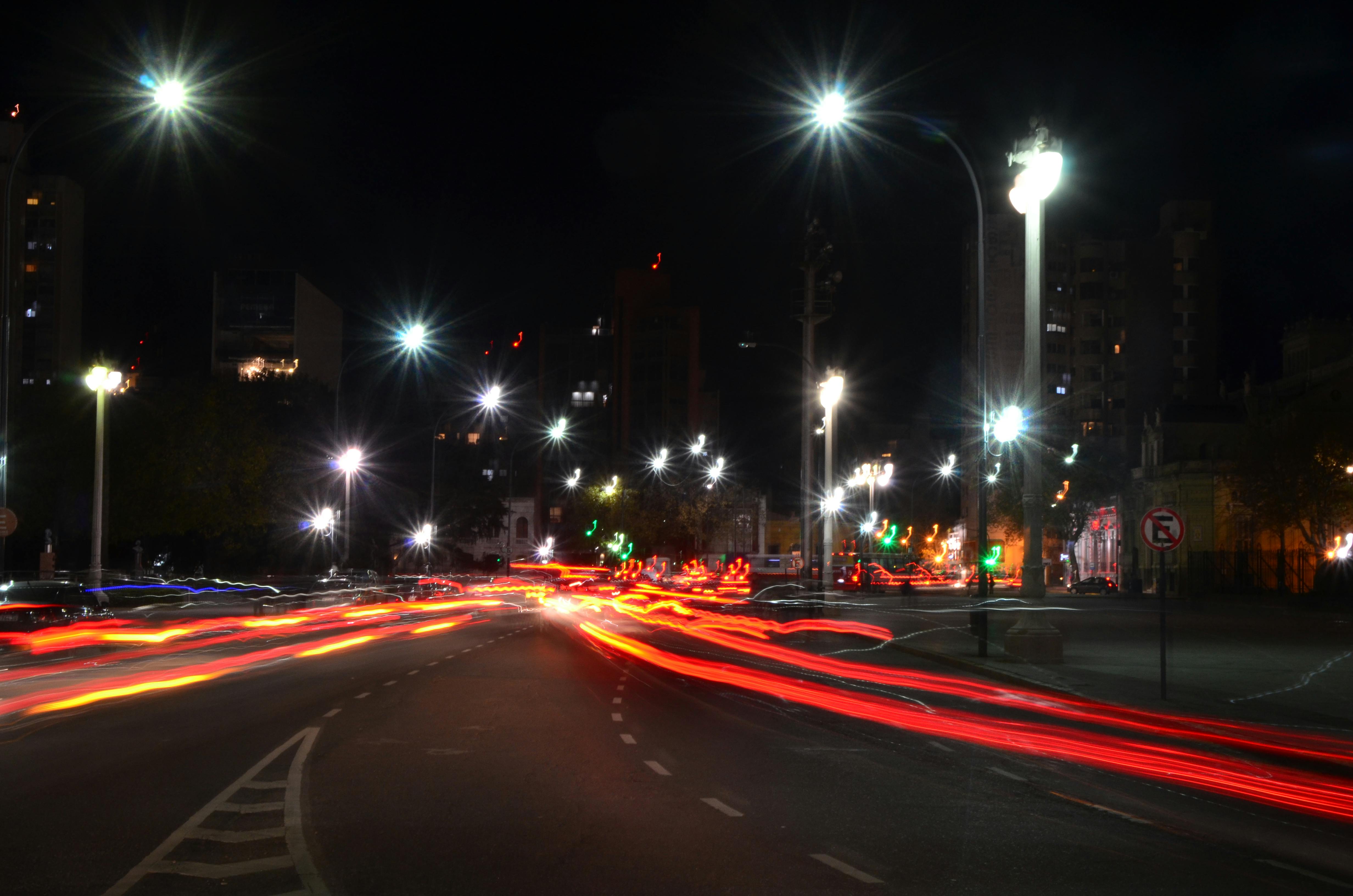 無料 夜の活気あふれる街並み。走る車や街灯から放たれる色とりどりの光の軌跡が美しい。 写真素材