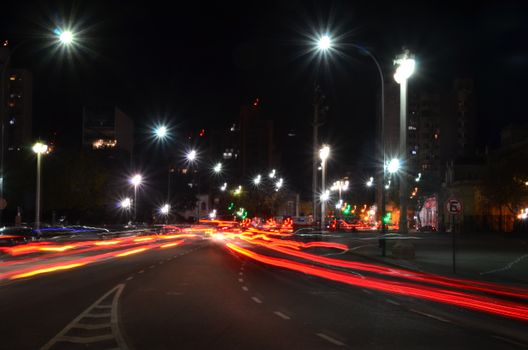 Vibrant city street at night with colorful light trails from moving vehicles and illuminated streetlights.