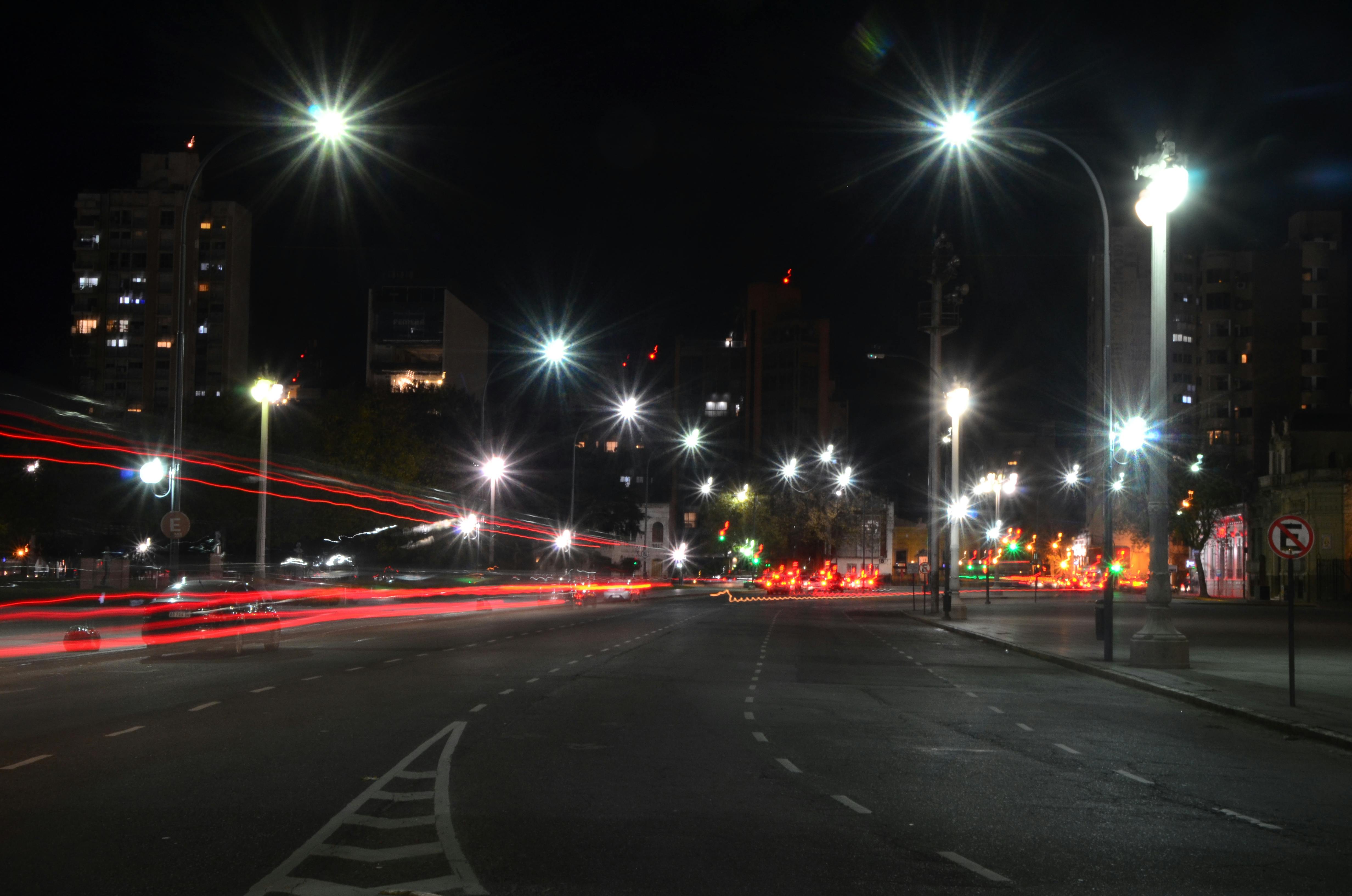 無料 光の軌跡と明るい街灯が人影のない道を照らし出す、ドラマチックな夜の街の風景。 写真素材