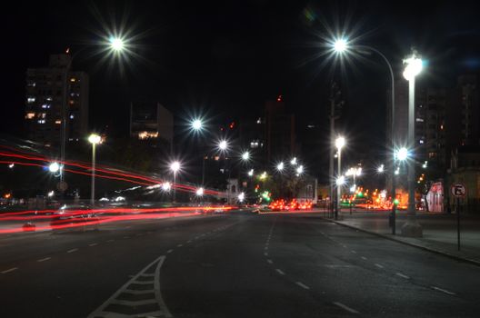 Dramatic nighttime city scene with light trails and bright streetlights illuminating an empty road.