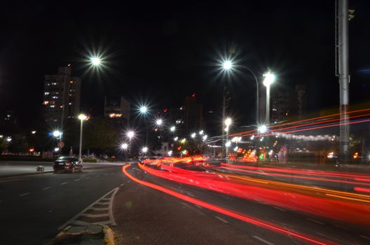 Vibrant night scene capturing car light trails and urban skyline with bright streetlights.