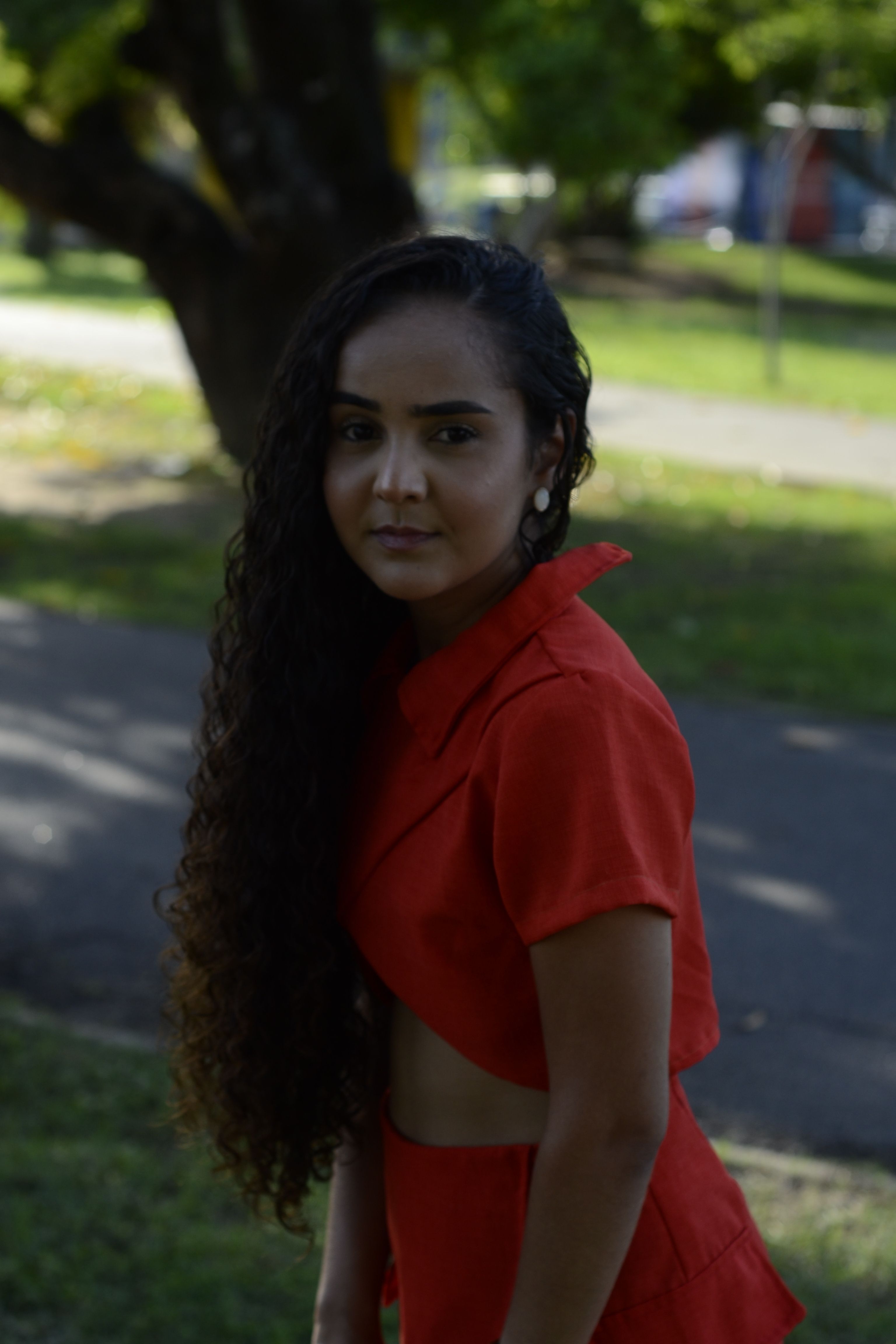 Woman with long curly hair wearing red dress in a park setting.