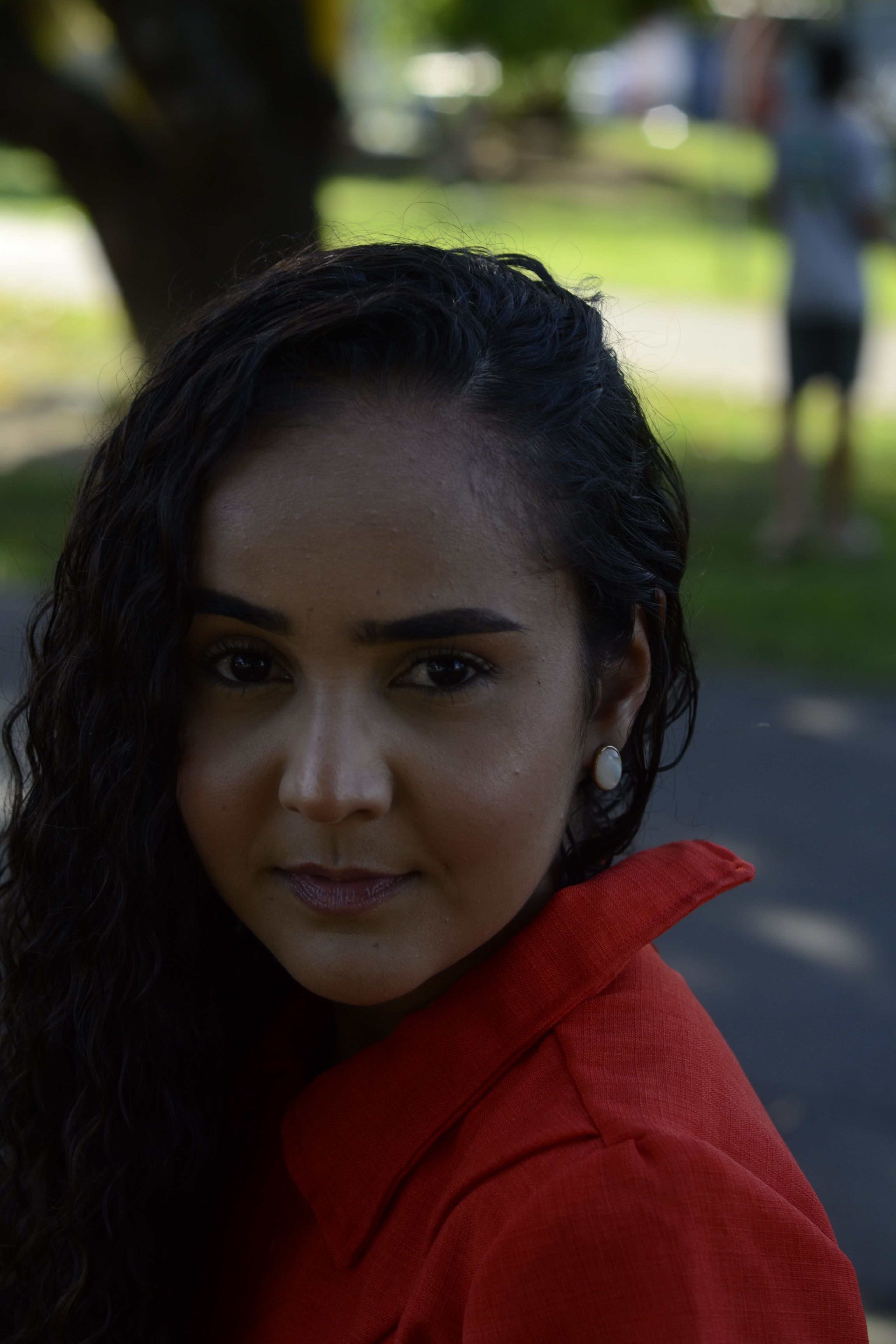 Close-up portrait of a woman with curly hair in a red jacket outdoors.