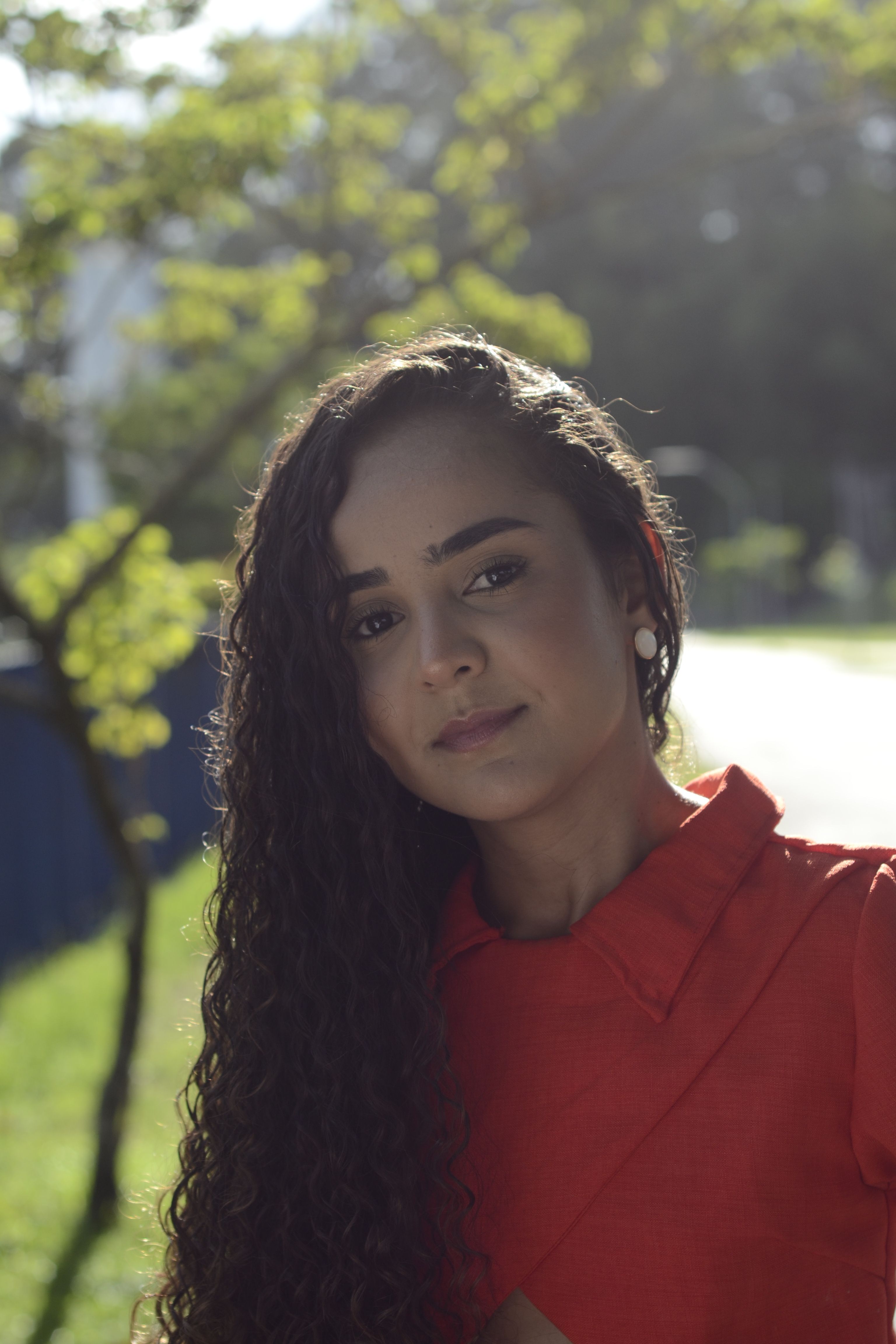 A young woman poses confidently in a red outfit, bathed in natural sunlight.