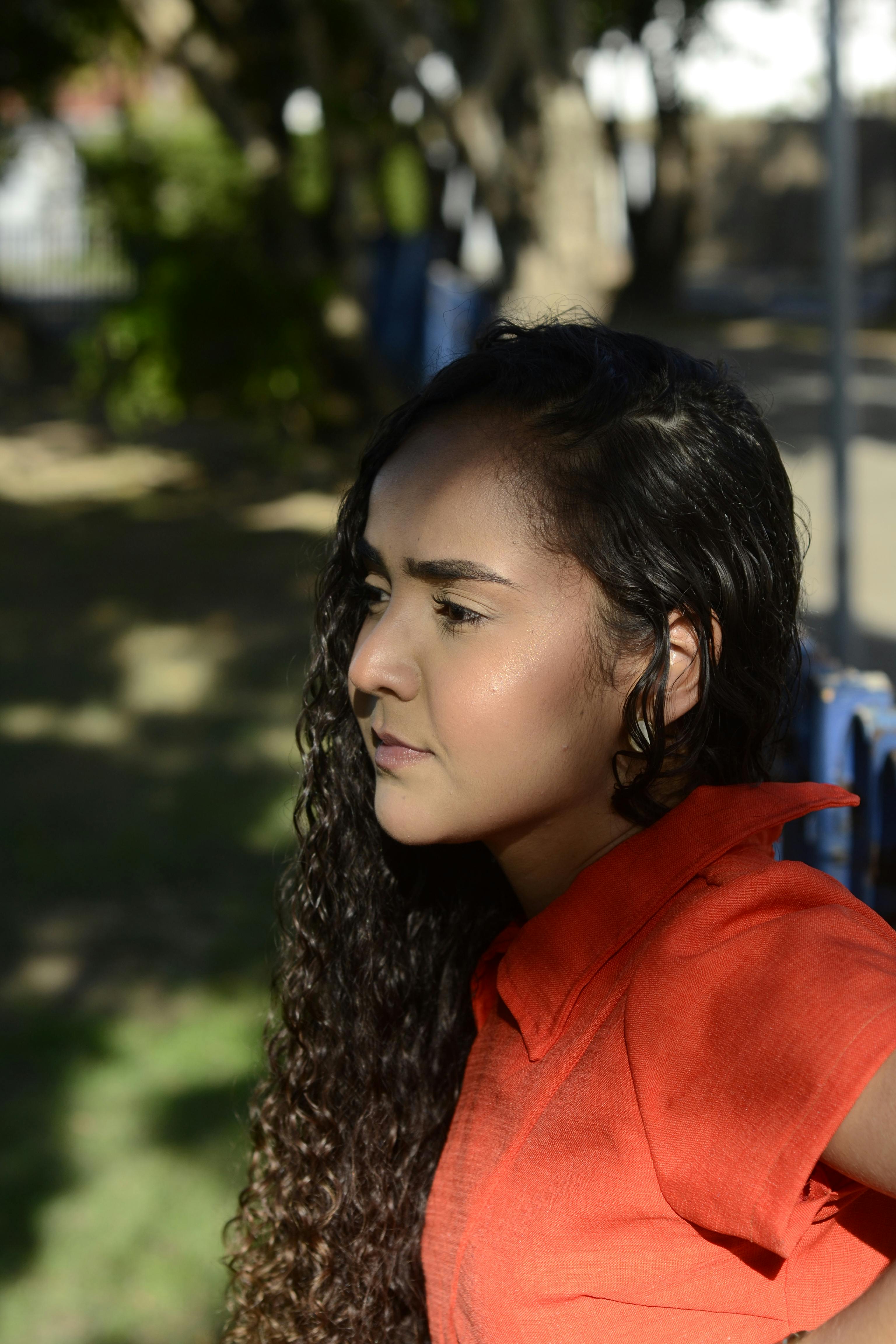 Gratis Profilo di una giovane donna con i capelli ricci e una maglietta rossa, fotografata all'aperto con luce naturale. Foto a disposizione