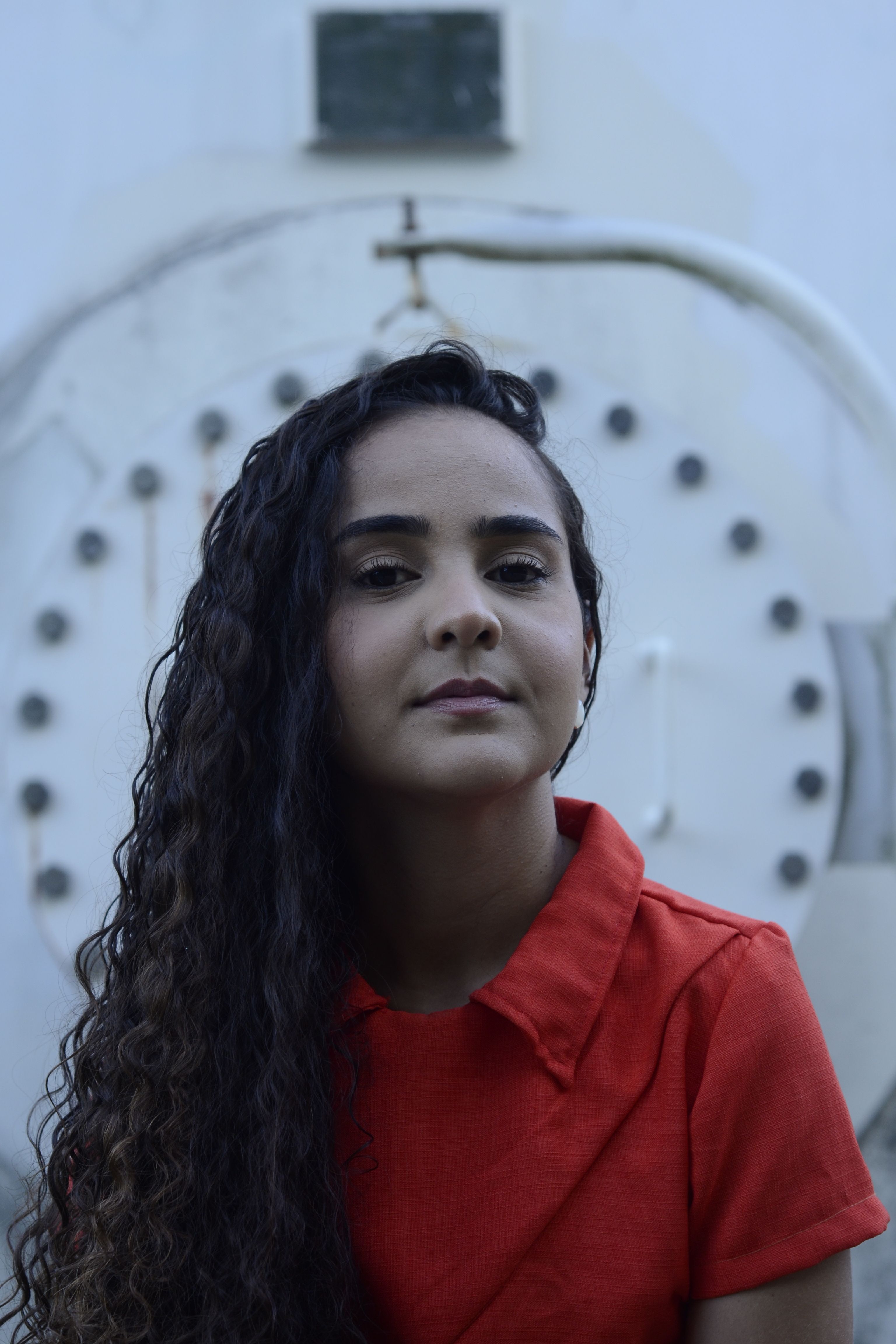 Young woman in red dress posing outdoors against industrial background.