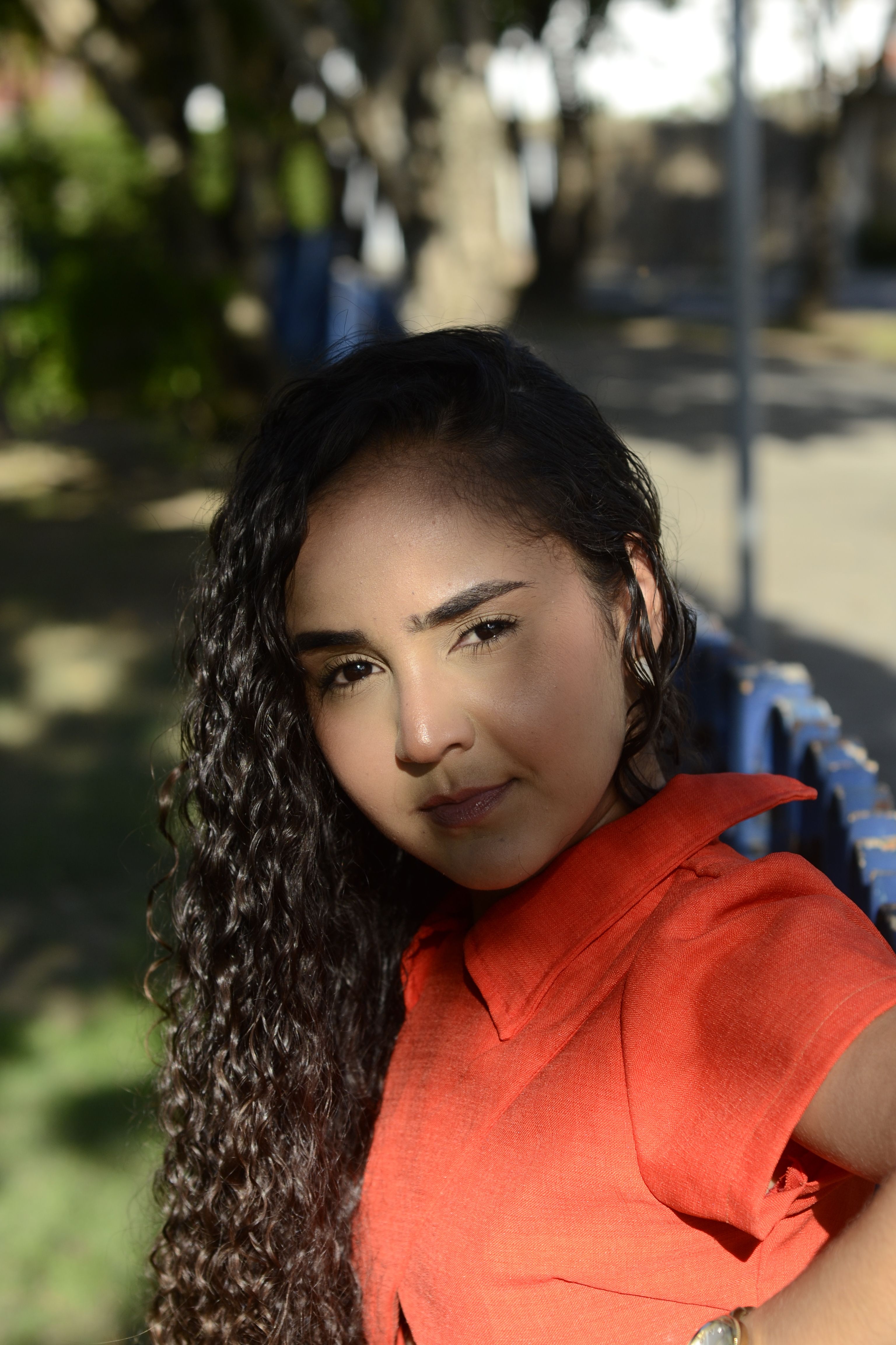 Portrait of a woman with curly hair outdoors in sunlight casting shadows.