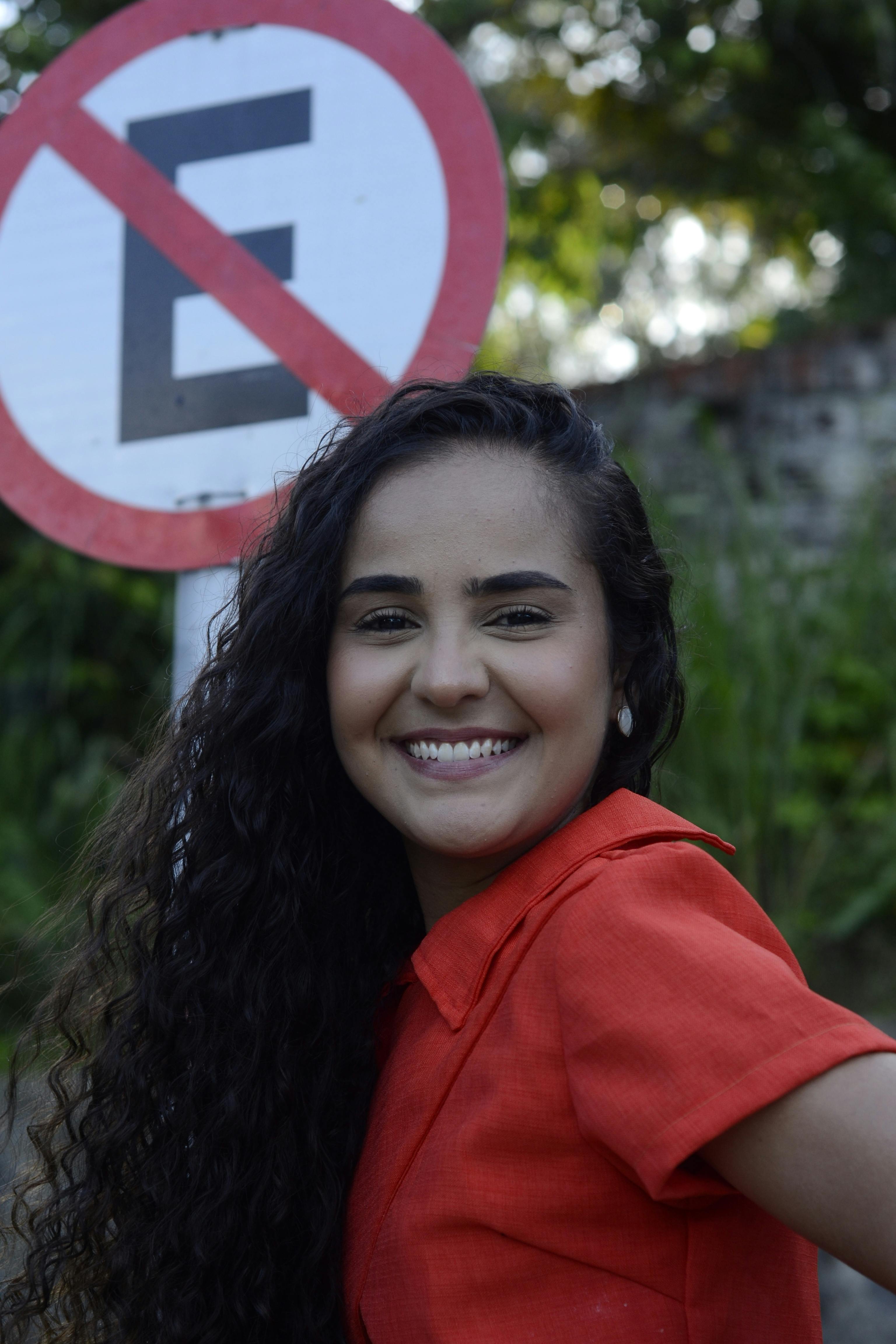 Cheerful woman in a red shirt posing near a no parking sign outdoors, expressing happiness and positivity.