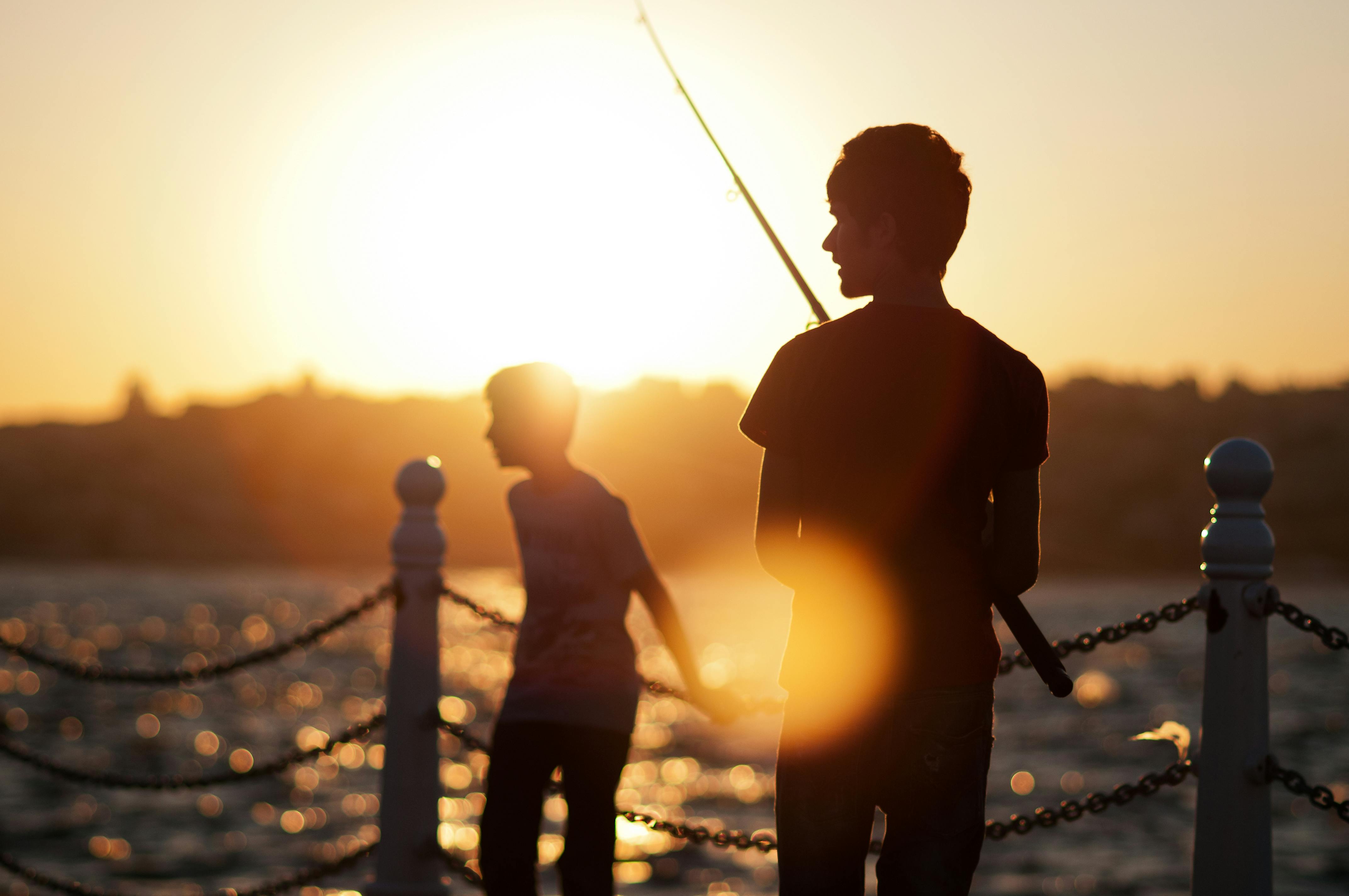 ฟรี เด็กชายสองคนกำลังตกปลาในยามพระอาทิตย์ตกดินริมชายฝั่งในอิสตันบูล ภาพเงาที่ปรากฏนั้นดูสงบและงดงาม คลังภาพถ่าย