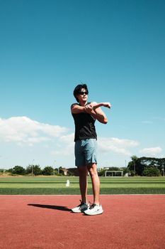 A man stretches his arms on an athletic track in Taytay, Philippines, under a clear blue sky.