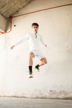 Dynamic action shot of an athlete jumping indoors in white sportswear.