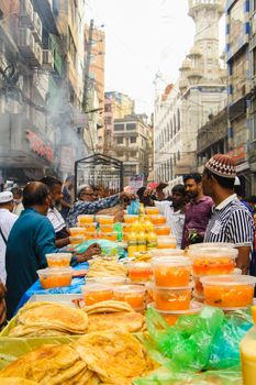 A bustling street market in Dhaka with people buying traditional iftar items during Ramadan.