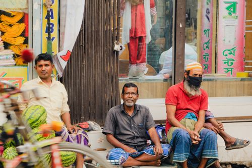 Free Three men sit with watermelons on a Dhaka street, showcasing daily life. Stock Photo