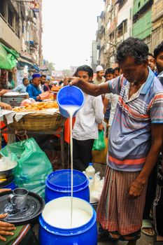 Crowded street market in Dhaka, Bangladesh, with a vendor pouring milk for customers.