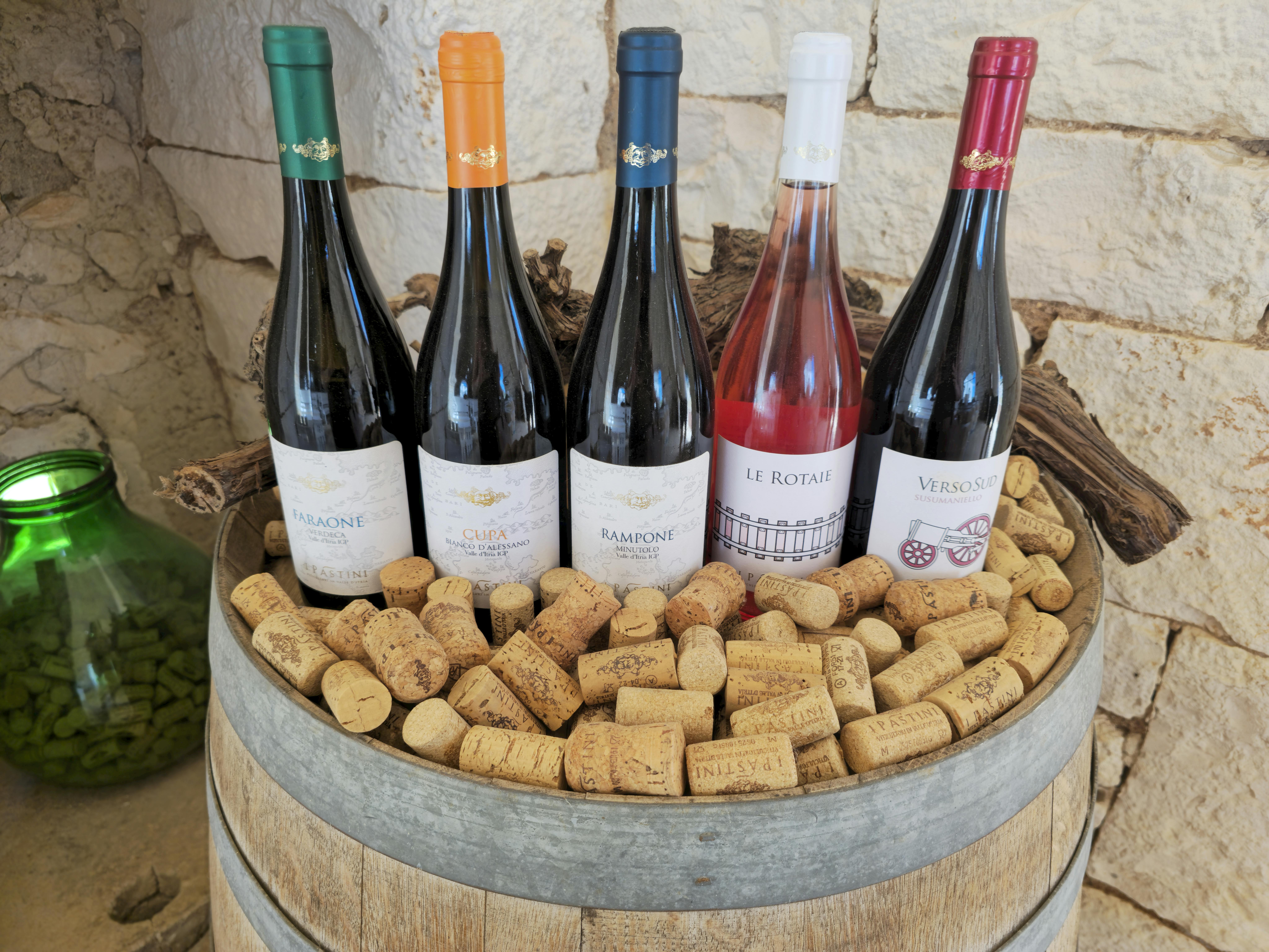 A rustic display of diverse wine bottles and corks on a barrel with a stone wall background.