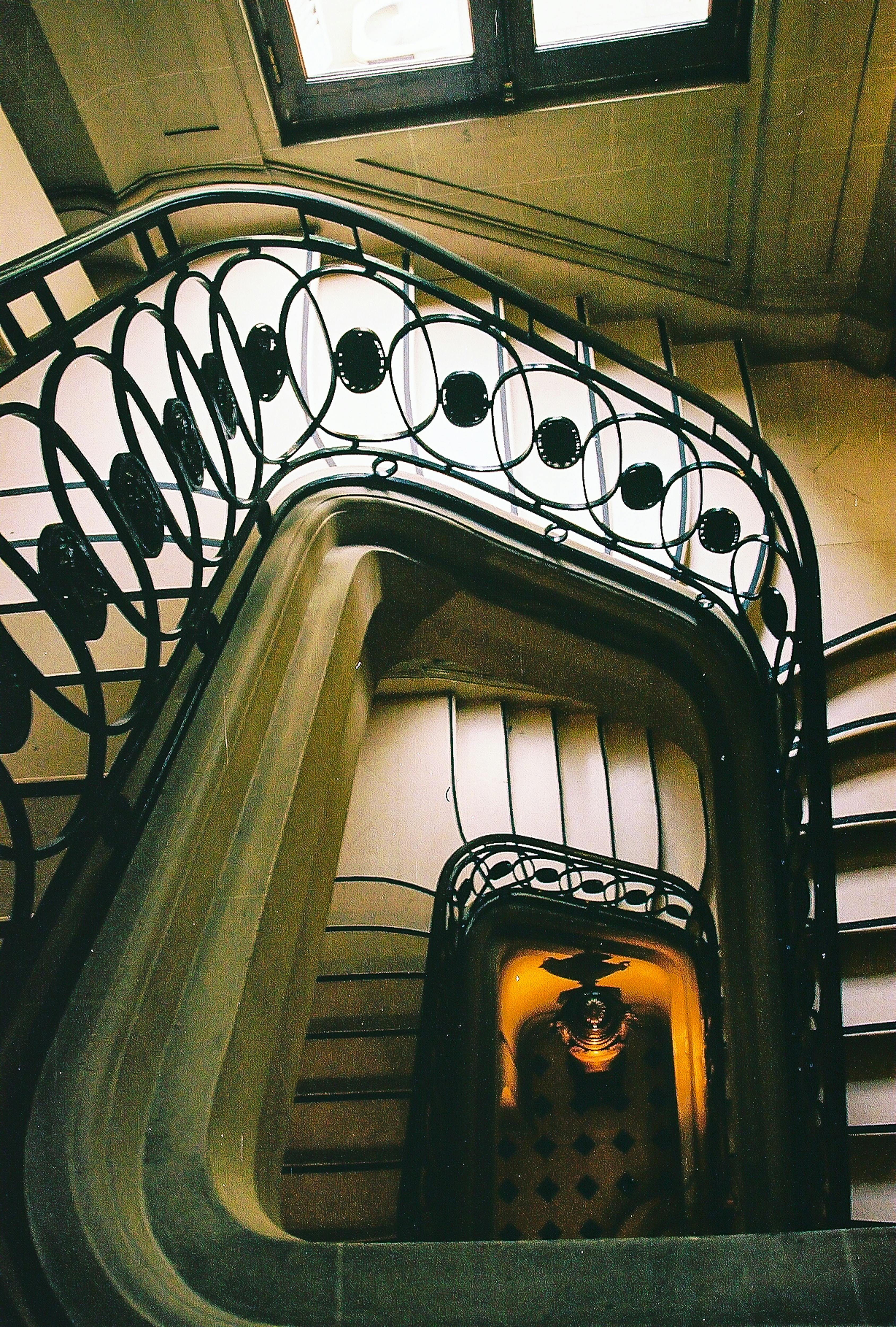 無料 歴史的建造物の中にある、装飾的な鉄製の手すりが付いた、趣のある螺旋階段を上から眺めた写真。 写真素材