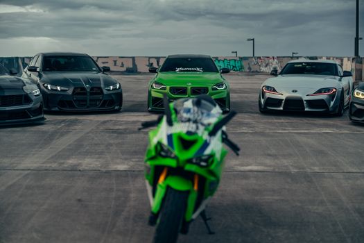 A striking image of luxury sports cars and a motorcycle on an urban rooftop with a moody sky.