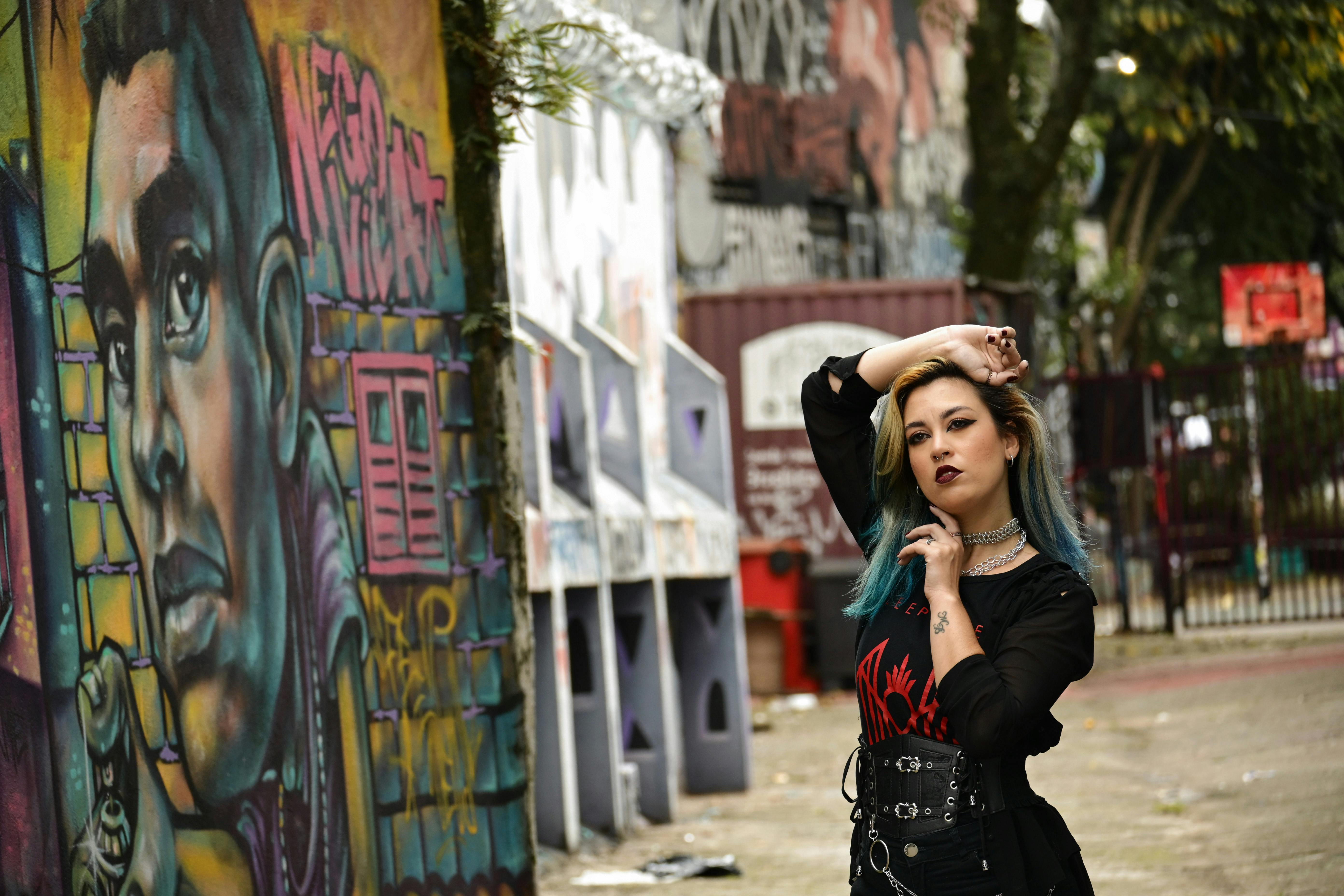 Gratis En stilig kvinne poserer selvsikkert foran livlig urban graffitikunst utendørs. Arkivbilde