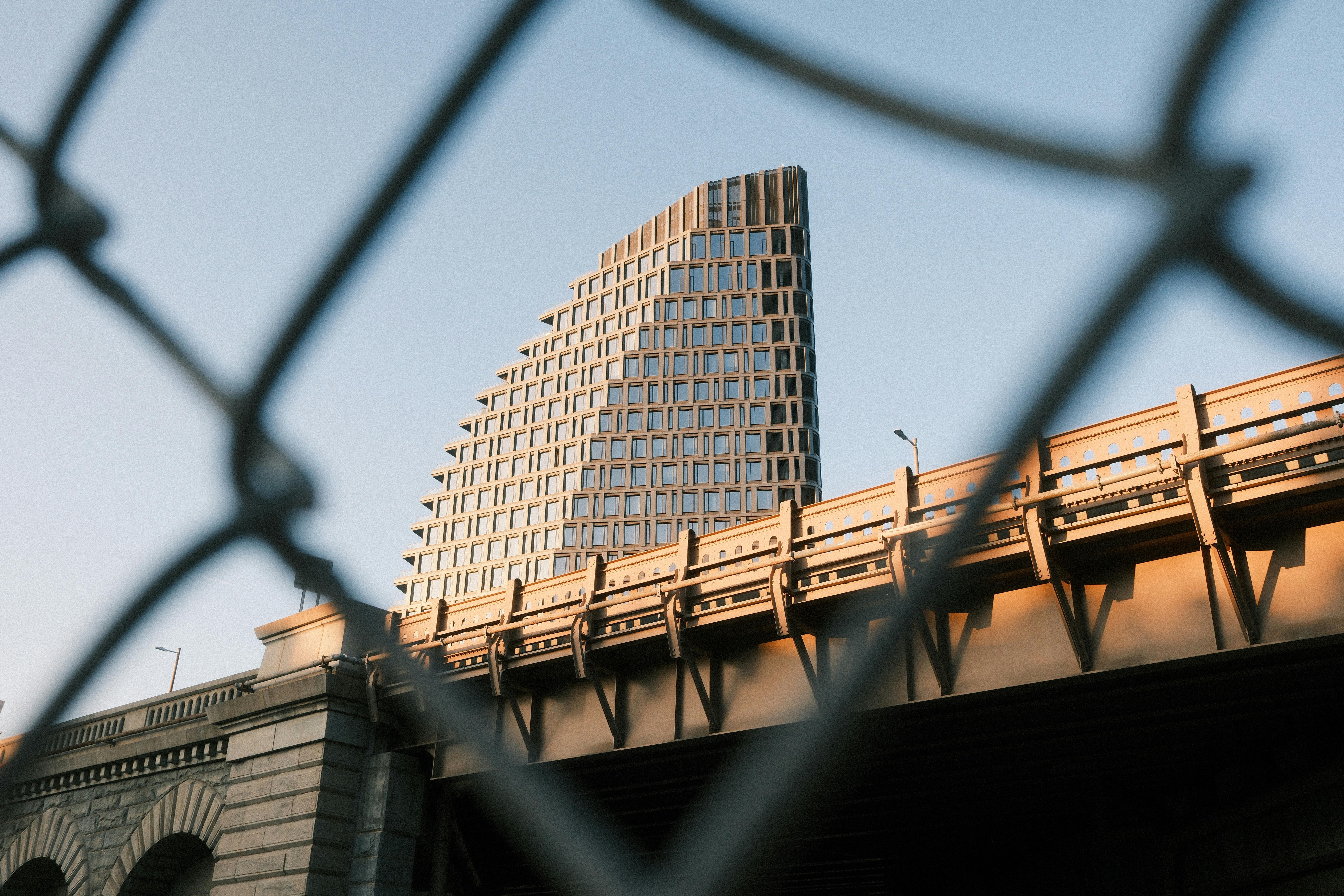 無料 金網フェンス越しに見える近代的な建物の建築的な眺め。日中の光の中で、都市の本質を捉えている。 写真素材