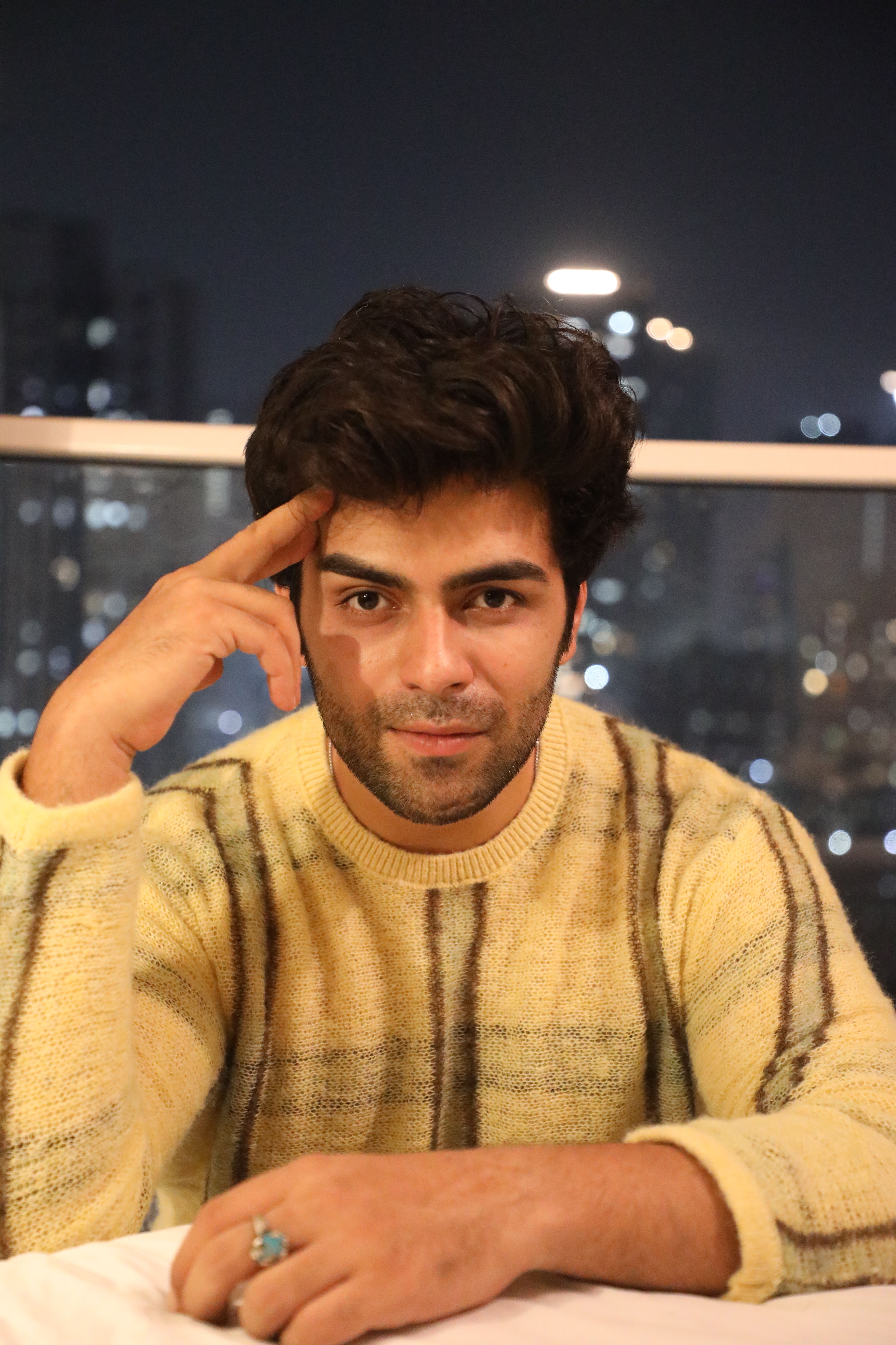 Portrait of a man in a striped sweater at night with a city skyline backdrop.