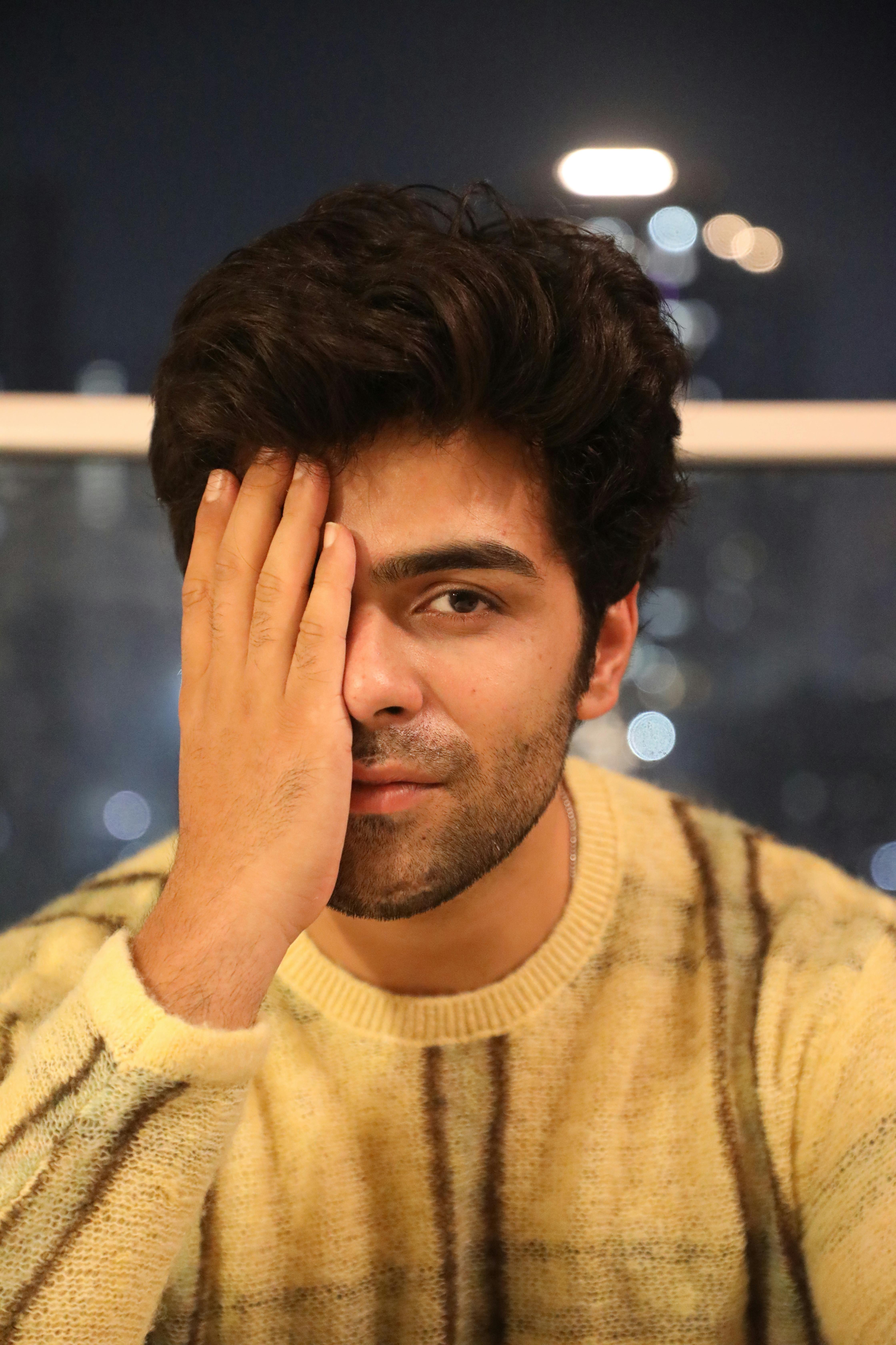 Portrait of a young man in a cozy sweater indoors, city lights in the background.