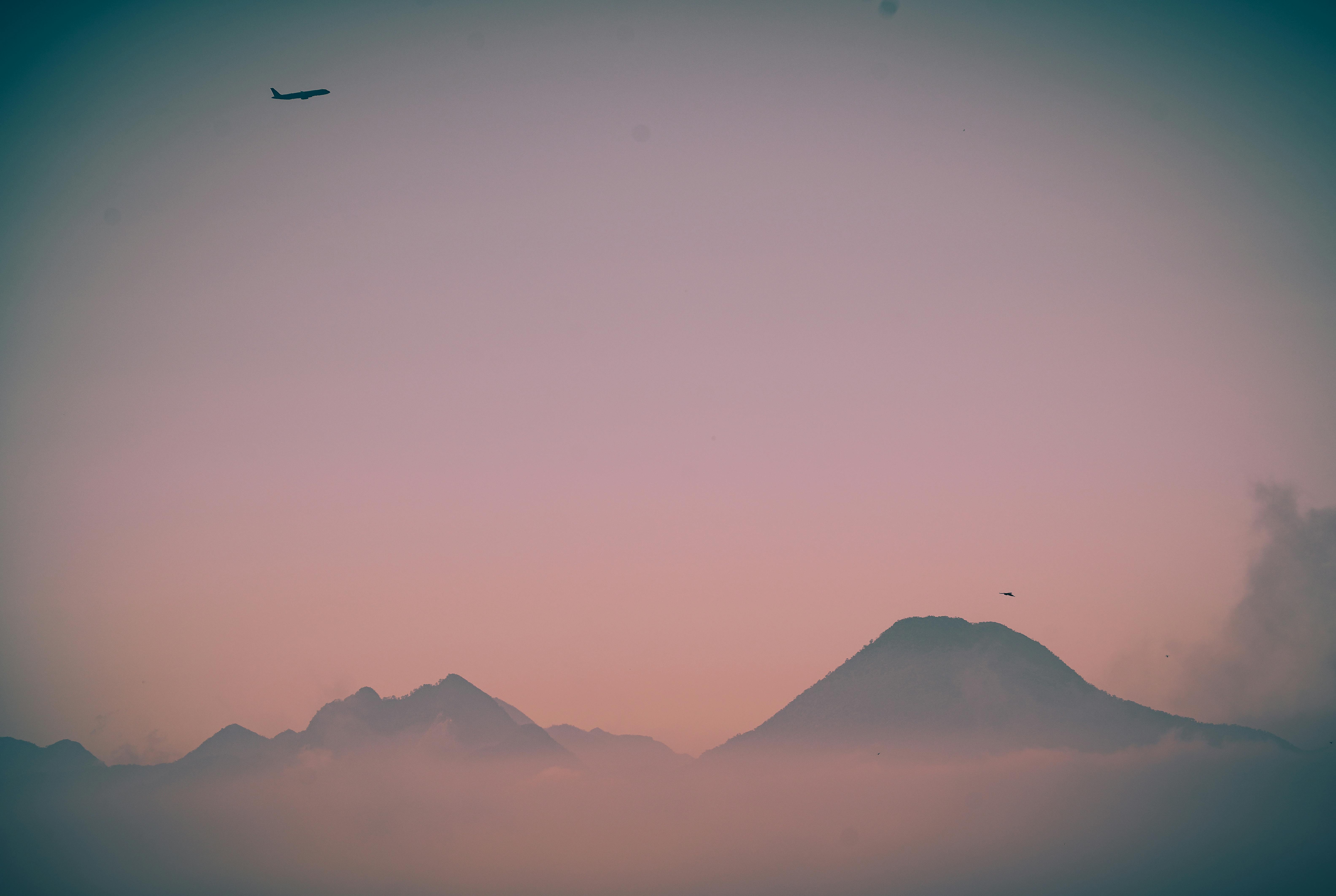 Gratis Un aereo sorvola montagne avvolte dalla nebbia durante un incantevole crepuscolo. Foto a disposizione