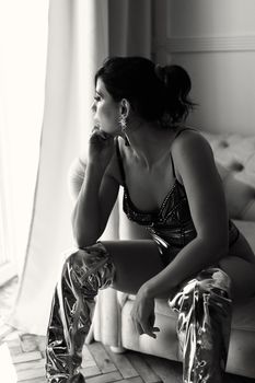Elegant black and white photo of a woman sitting in a reflective pose indoors.