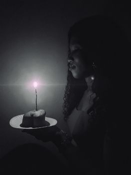 Moody black and white photo of a woman holding a birthday cake with candle lighting.