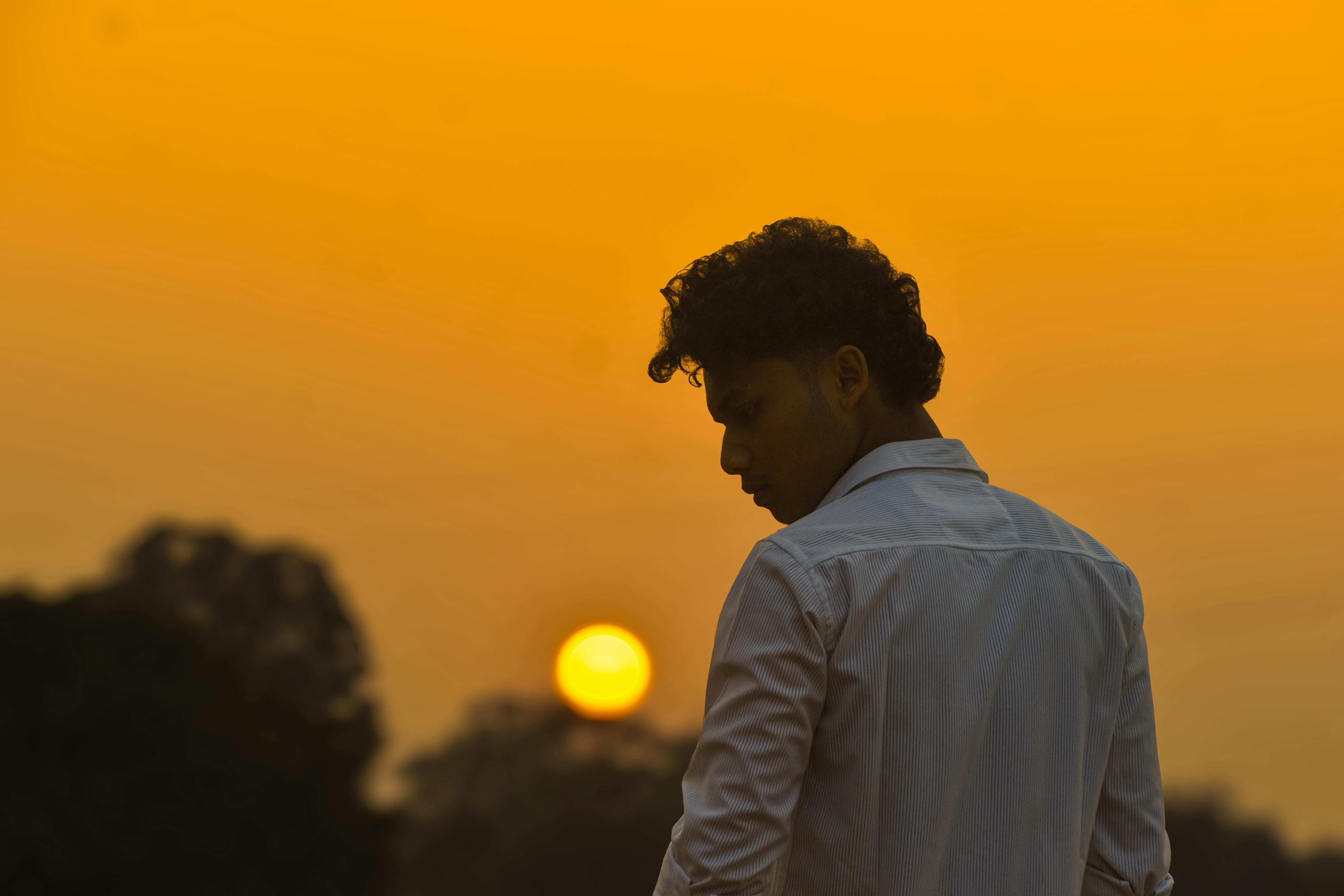 Δωρεάν Ένας άντρας με πουκάμισο κοιτάζει πάνω από τον ώμο του με φόντο ένα ζωντανό ηλιοβασίλεμα. Φωτογραφία από στοκ φωτογραφιών