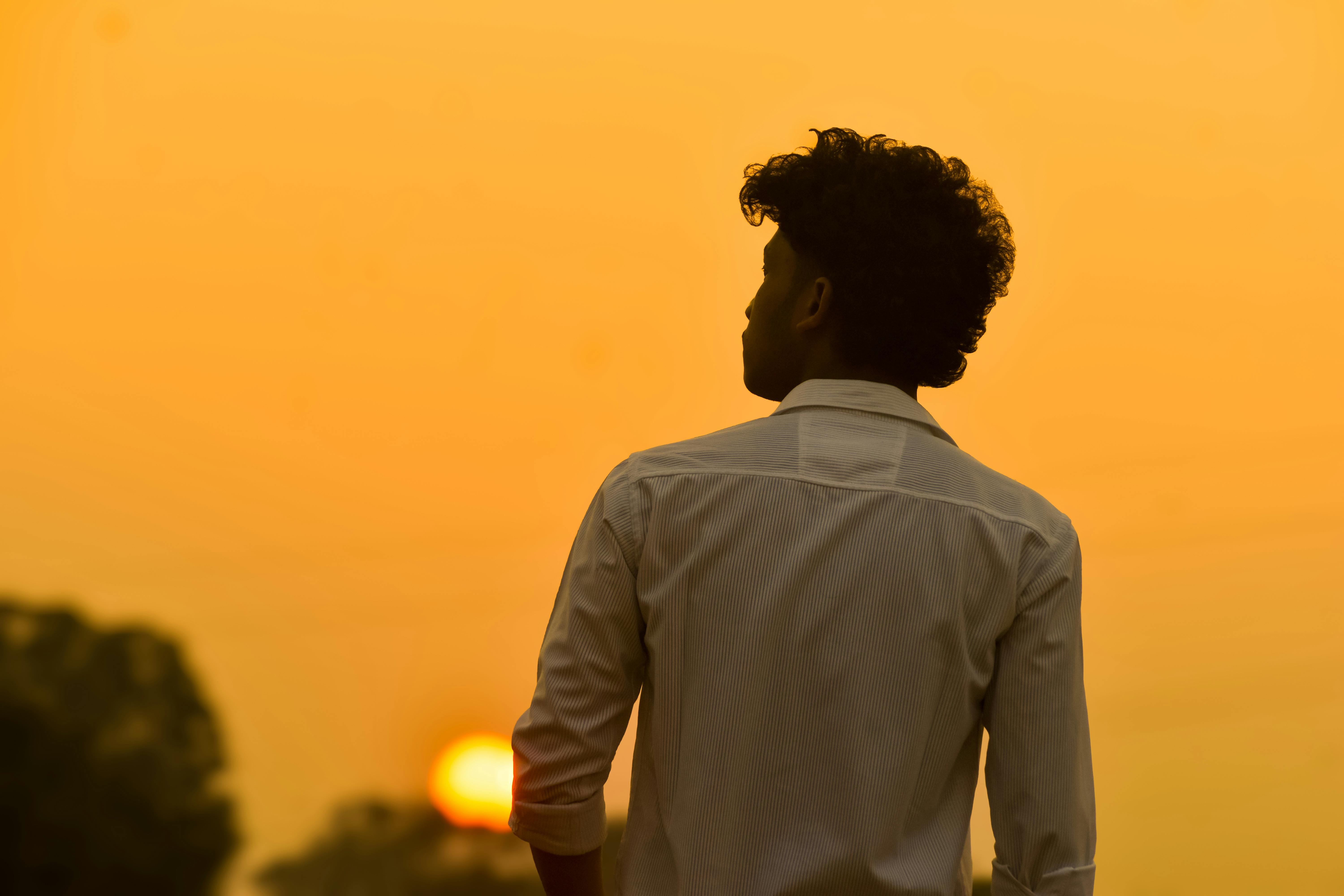 gratis Het silhouet van een man die over het leven nadenkt tegen een levendige oranje zonsondergang. Stockfoto