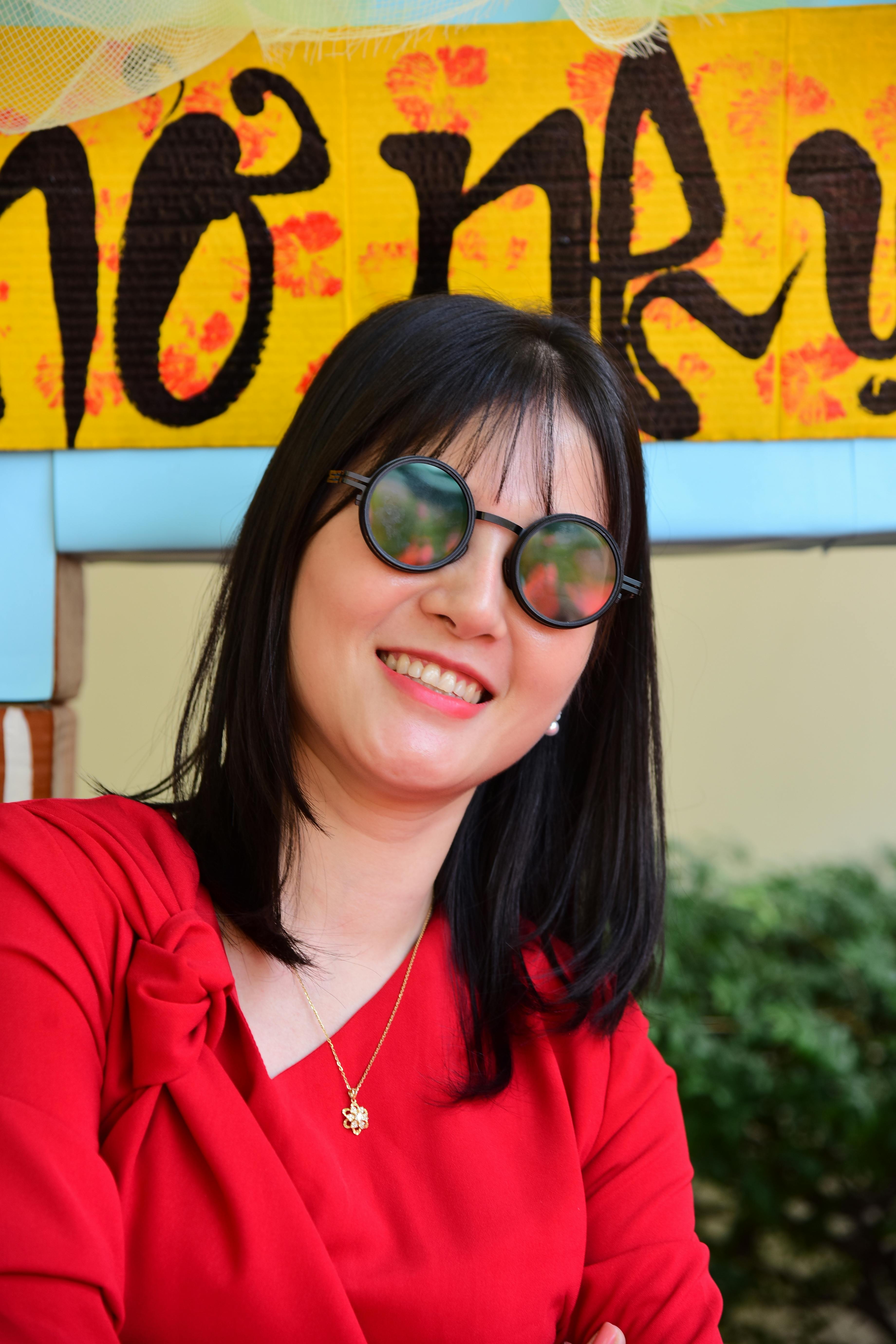 Smiling woman in red with sunglasses against a colorful backdrop. Perfect for lifestyle and fashion themes.