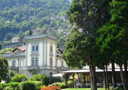 Beautiful villa amidst lush greenery in Lombardy, Italy, with scenic hill backdrop.