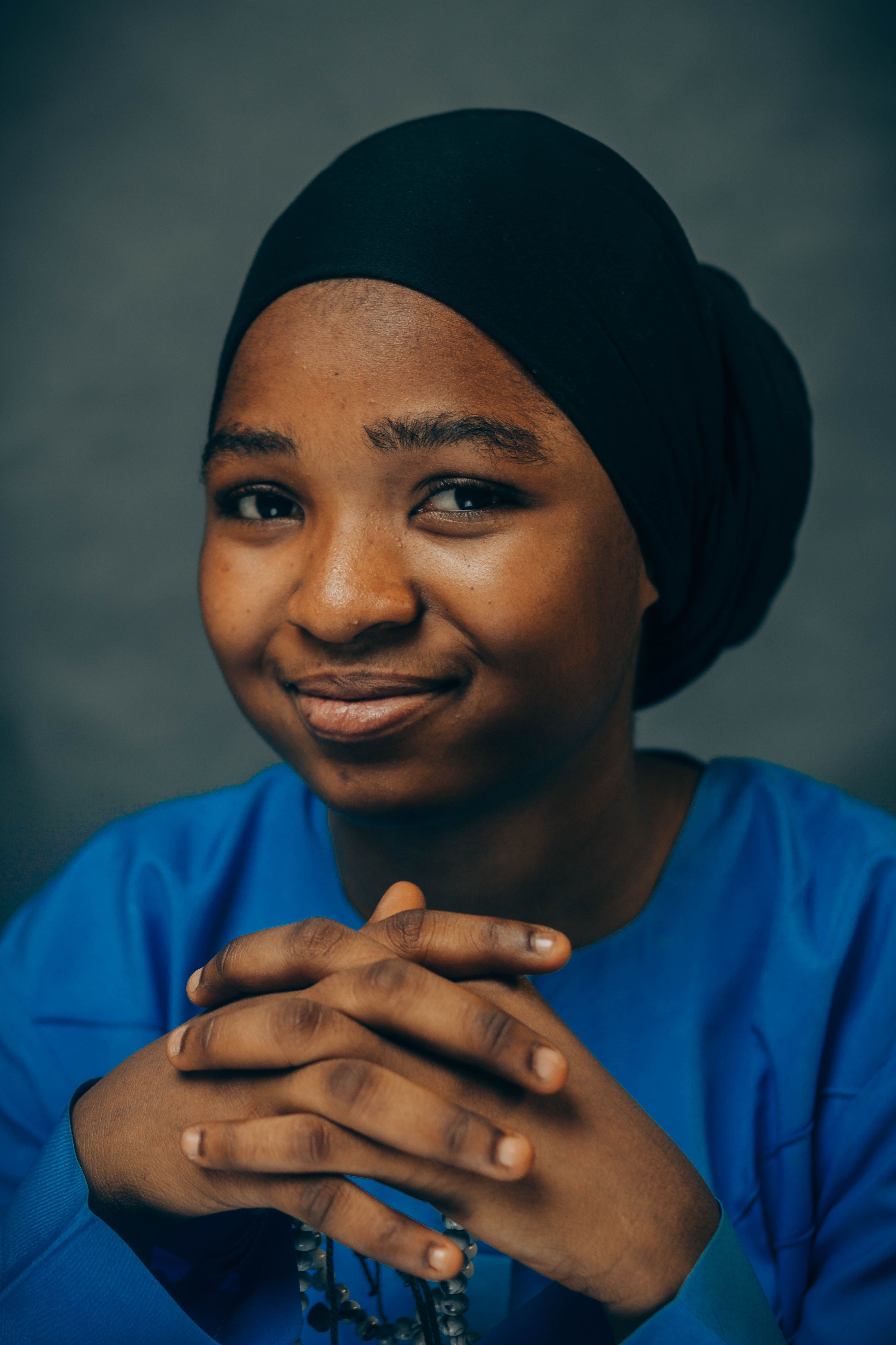Portrait of a young woman from Nigeria with a confident smile, wearing blue attire and a black hijab.