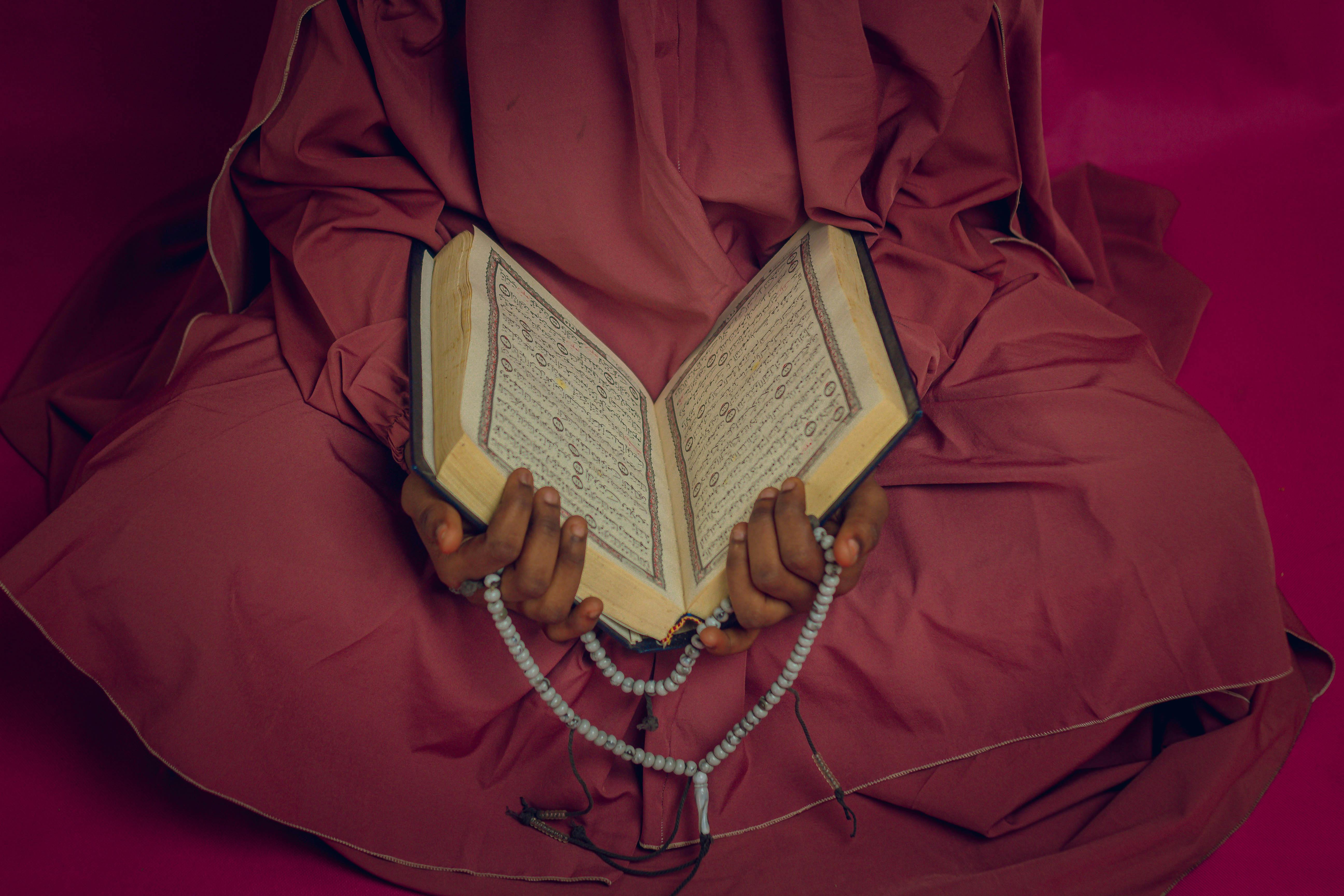 Zadarmo Žena oblečená v tradičnom odeve číta Korán a drží v ruke modlitebné korálky, čo odráža oddanosť a spiritualitu. Fotka z fotobanky