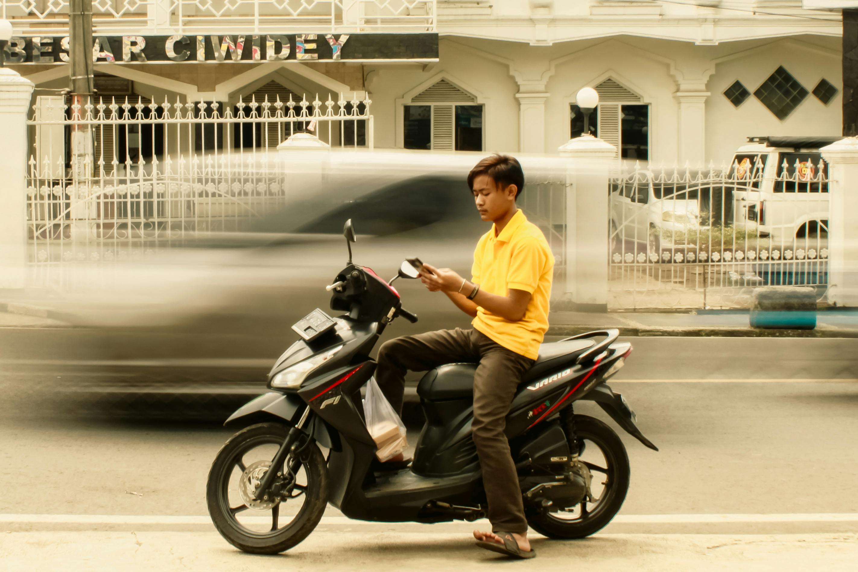 Kostnadsfria En ung man sitter på en skoter och läser medan han är parkerad vid en trafikerad gata. Stock foto