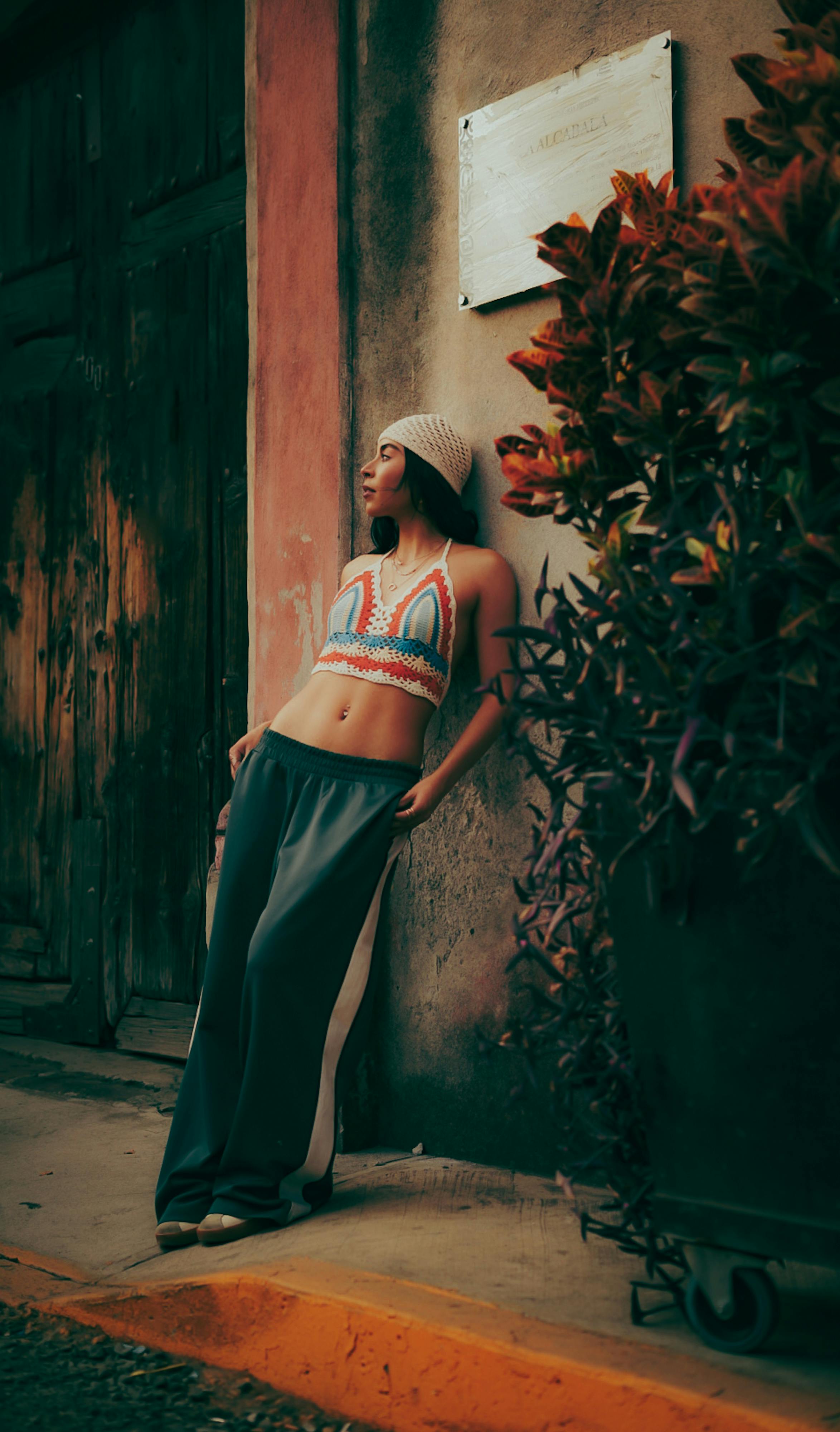 Gratuit Jeune femme détendue en tenue décontractée, appuyée contre un mur à côté d'une jardinière, dégageant une impression de sérénité. Photos