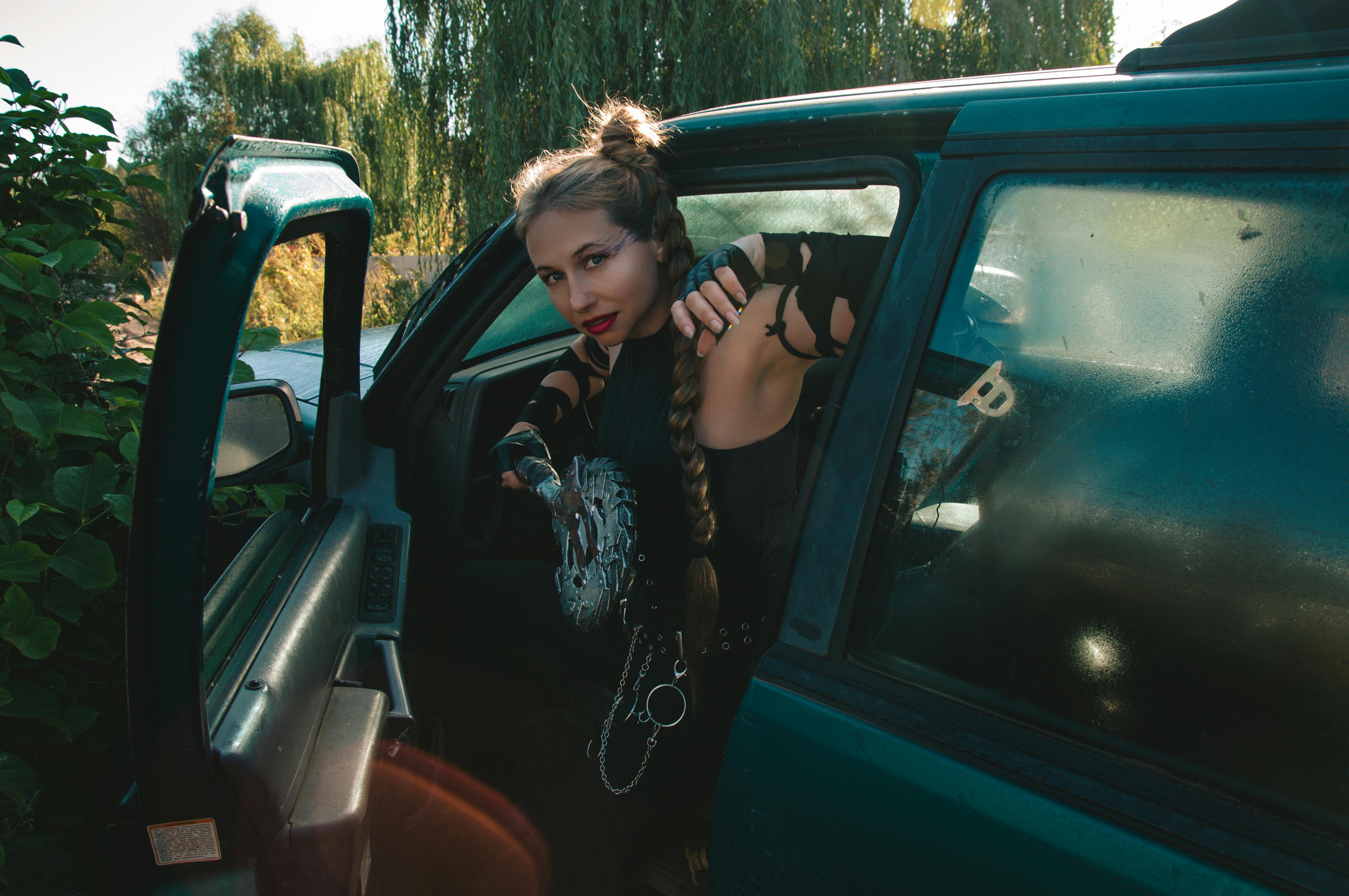 ingyenes Divatos, fonott hajú és egyedi öltözékű nő ​​száll ki egy autóból természetes környezetben, merész stílust képviselve. Stockfotó