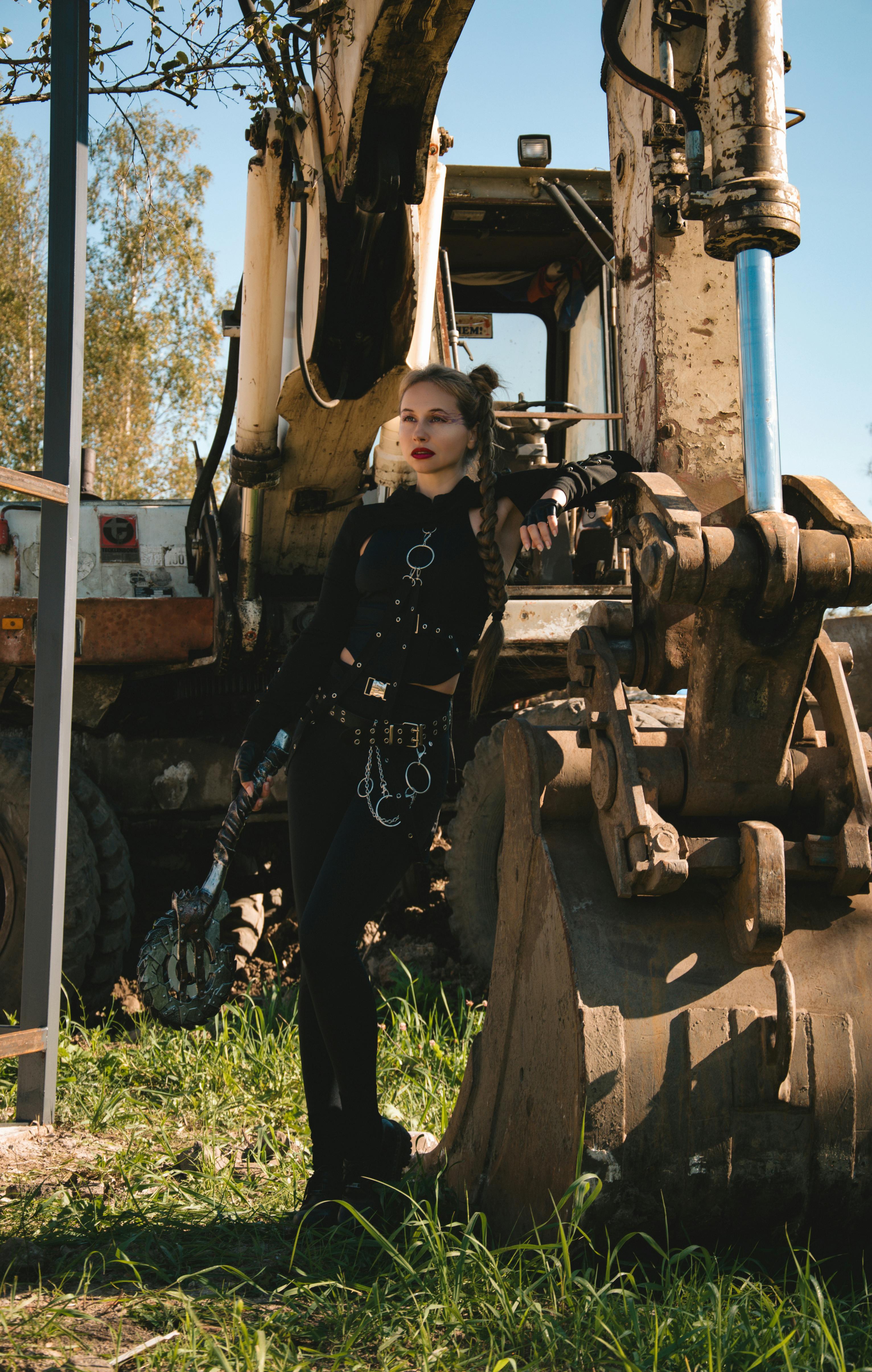 免费 阳光明媚的日子里，一位身着黑色时装的女子倚靠在挖掘机的铲斗上。 素材图片