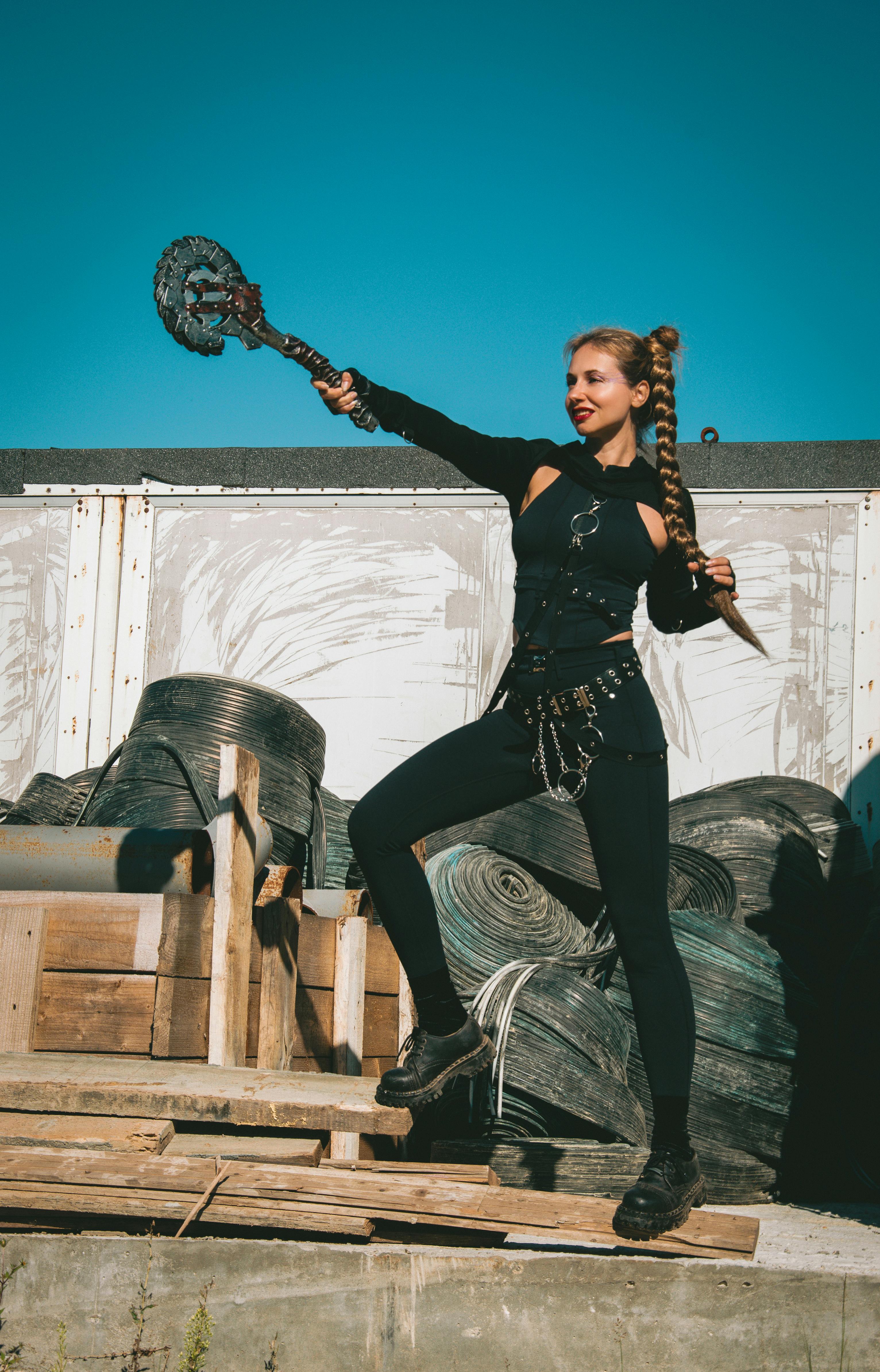 Bezpłatne Wojowniczka w czarnym stroju pozuje dynamicznie z bronią plemienną na zewnątrz. Zdjęcie z galerii