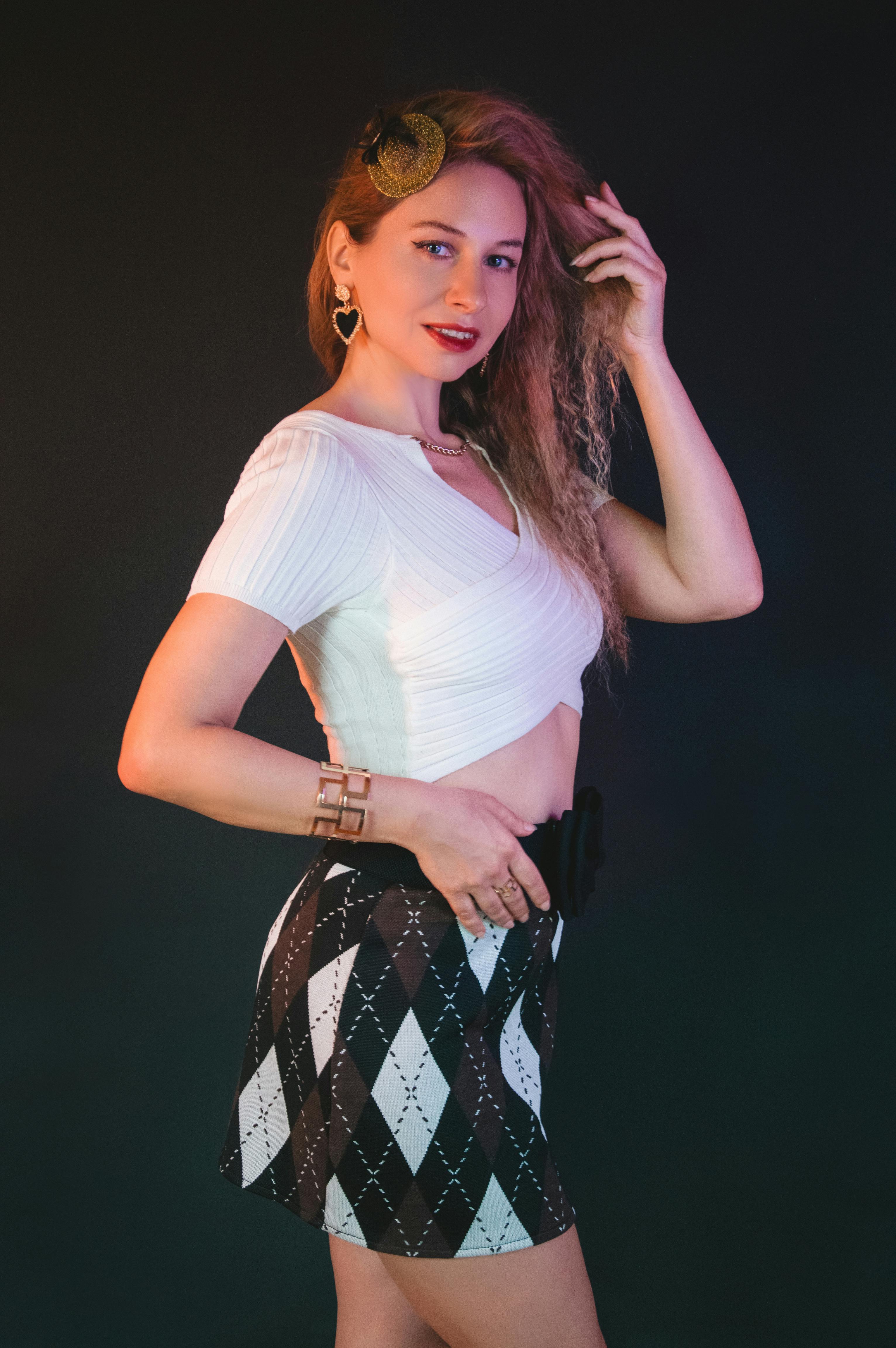 ingyenes Stílusos nő pózol magabiztosan argyle szoknyában és fehér felsőben sötét háttér előtt. Stockfotó