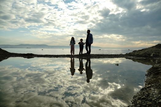 A family standing by water's edge with reflections and dramatic sky in Bursa.