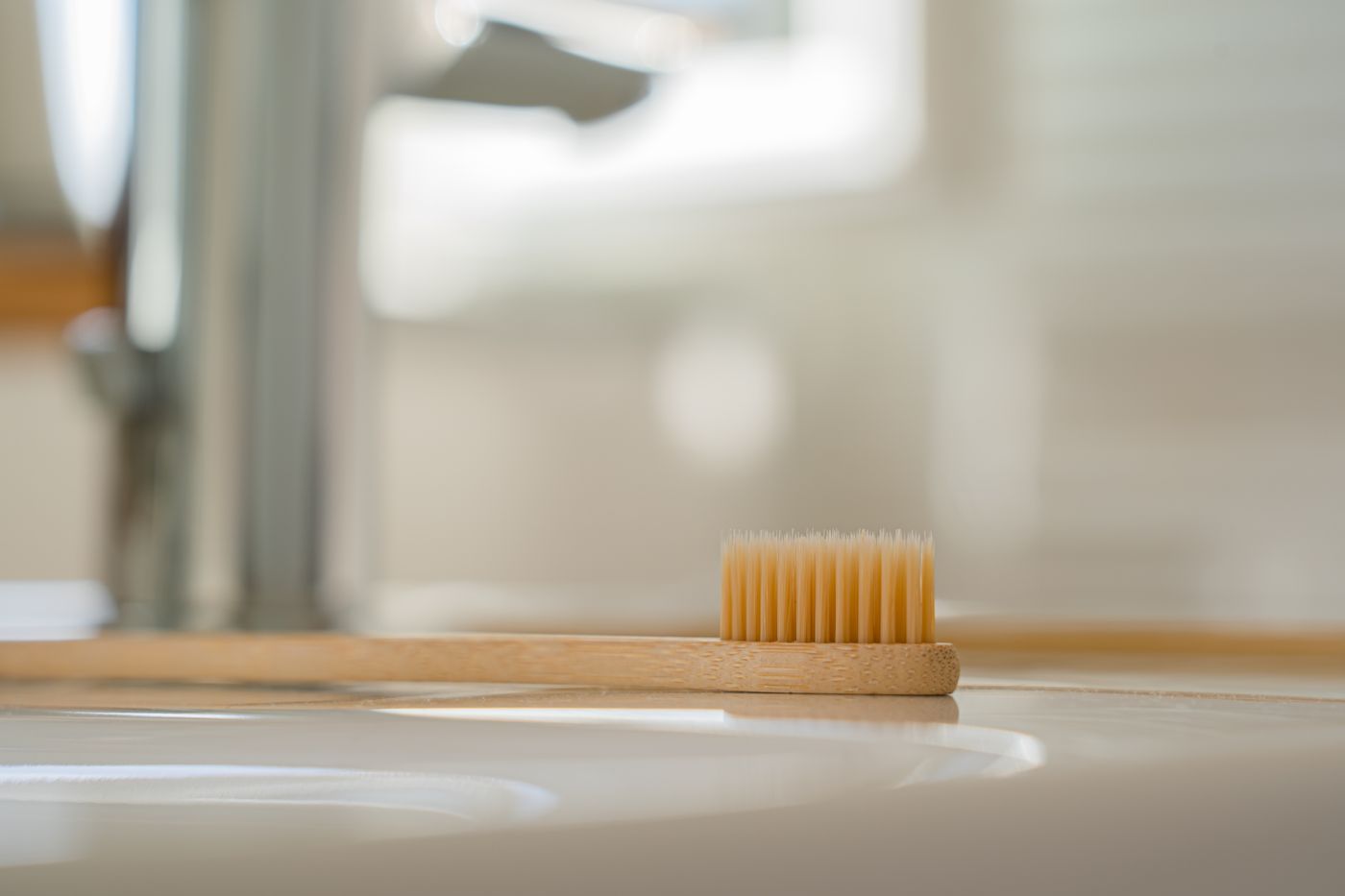 Bamboo toothbrush resting beside a bathroom sink as part of a clean oral-care routine