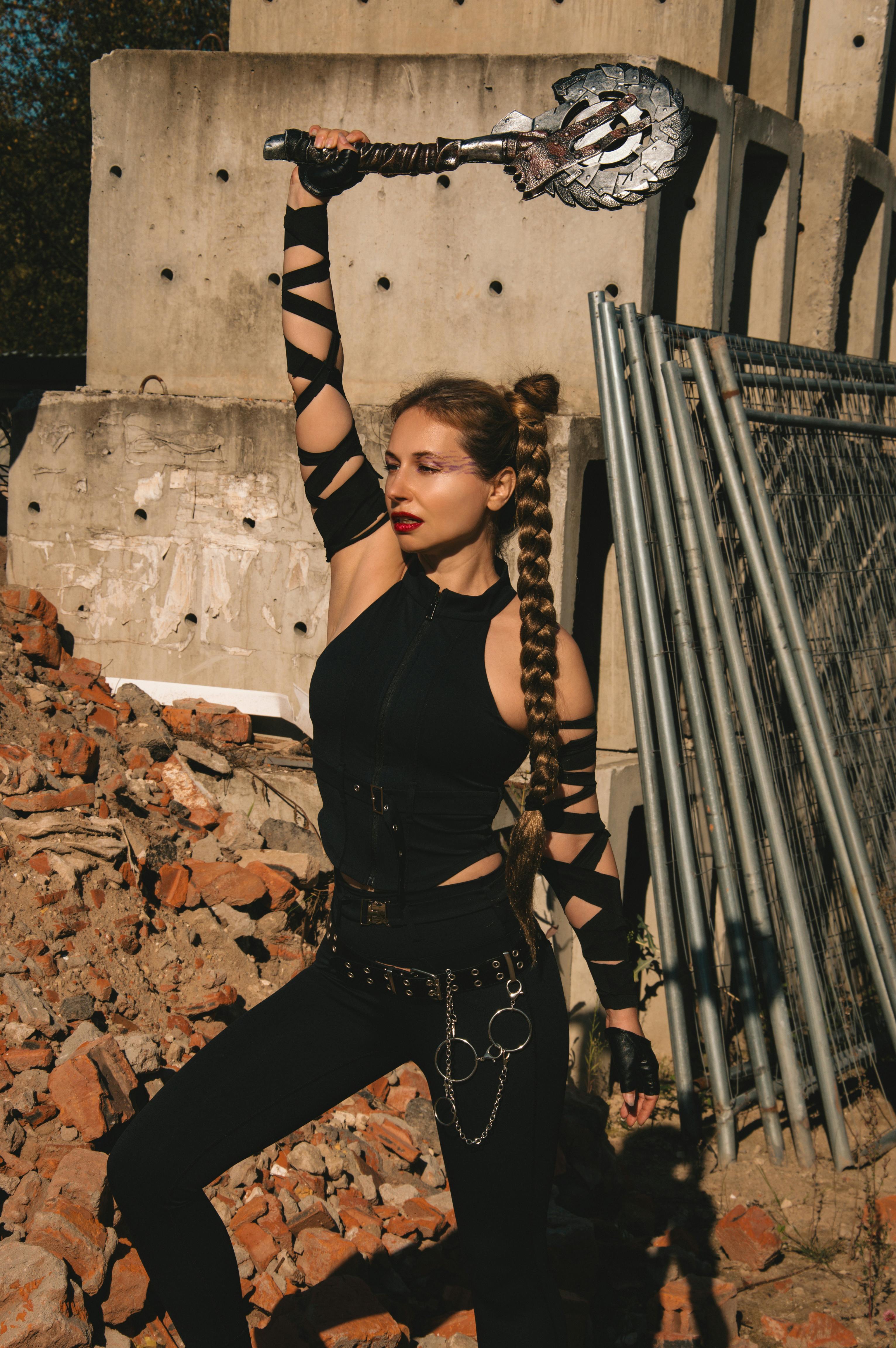 Kostnadsfria Våldsam kvinna i svart dräkt som svingar stridsyxa i en urban ruinmiljö. Stock foto