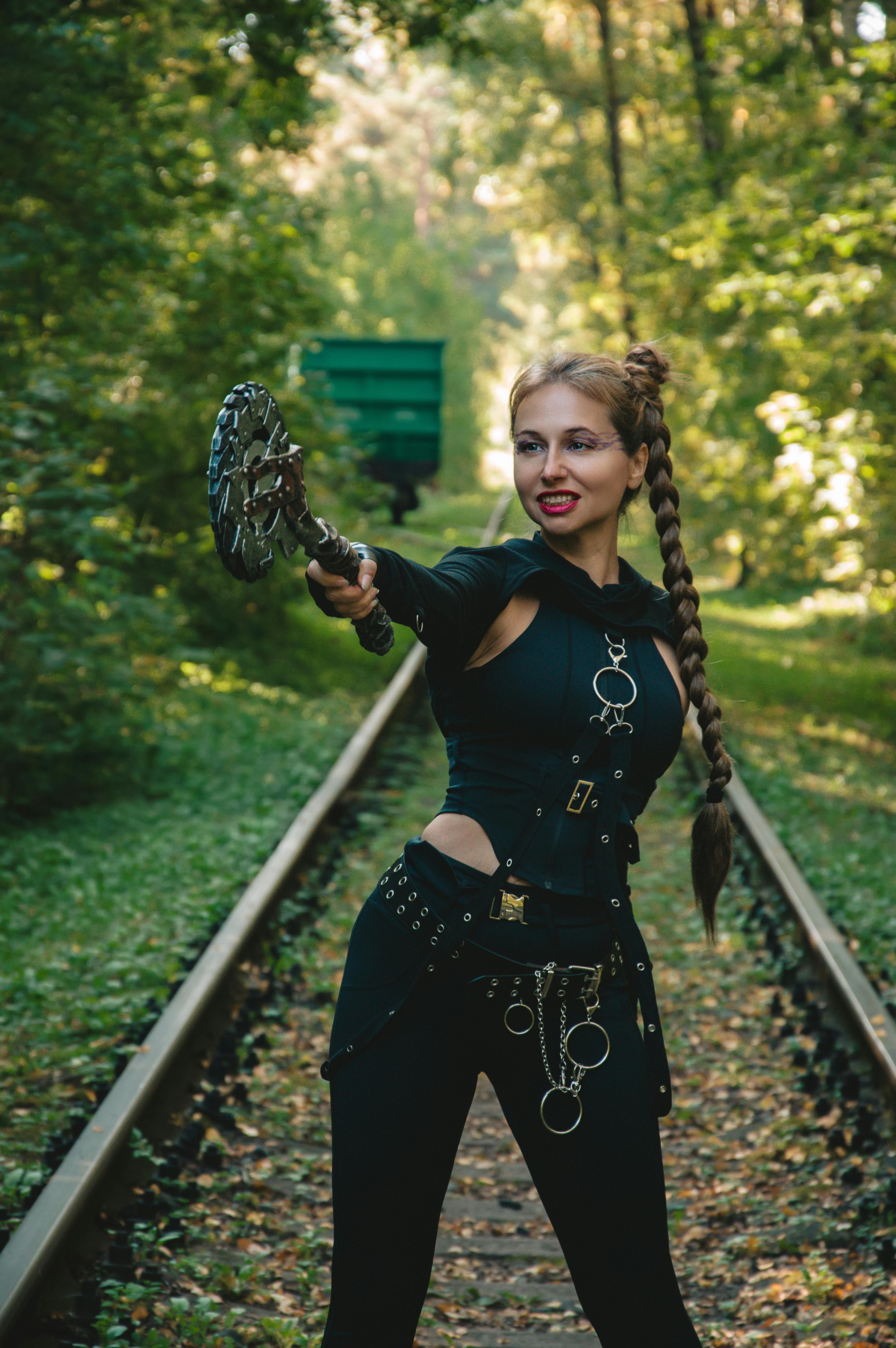 Gratuit Une guerrière redoutable pose avec une arme sur des voies ferrées au milieu d'une forêt verdoyante. Photos