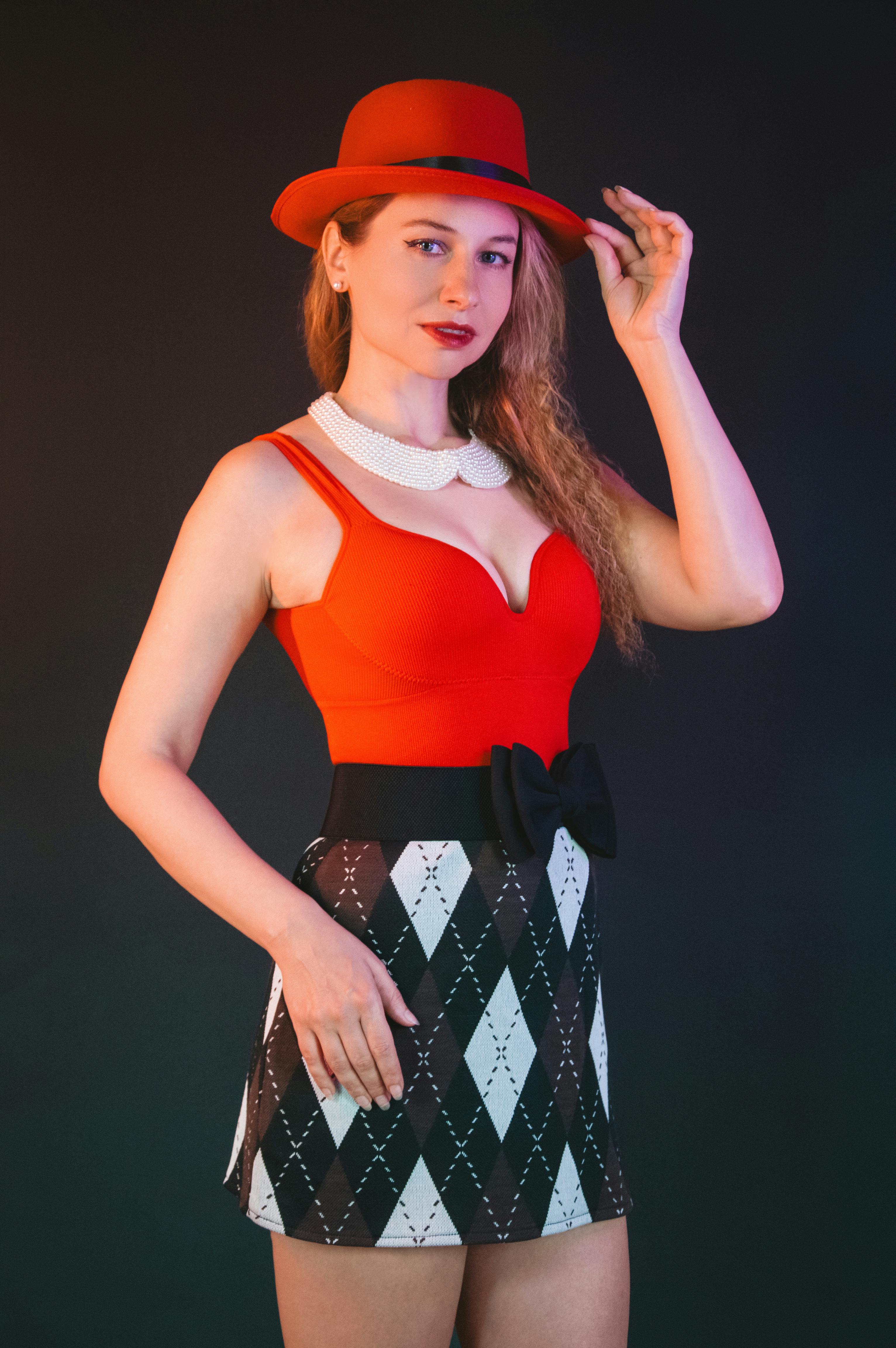 Kostnadsfria Modern kvinna med röd hatt och snygg outfit, poserar självsäkert mot en mörk bakgrund. Stock foto