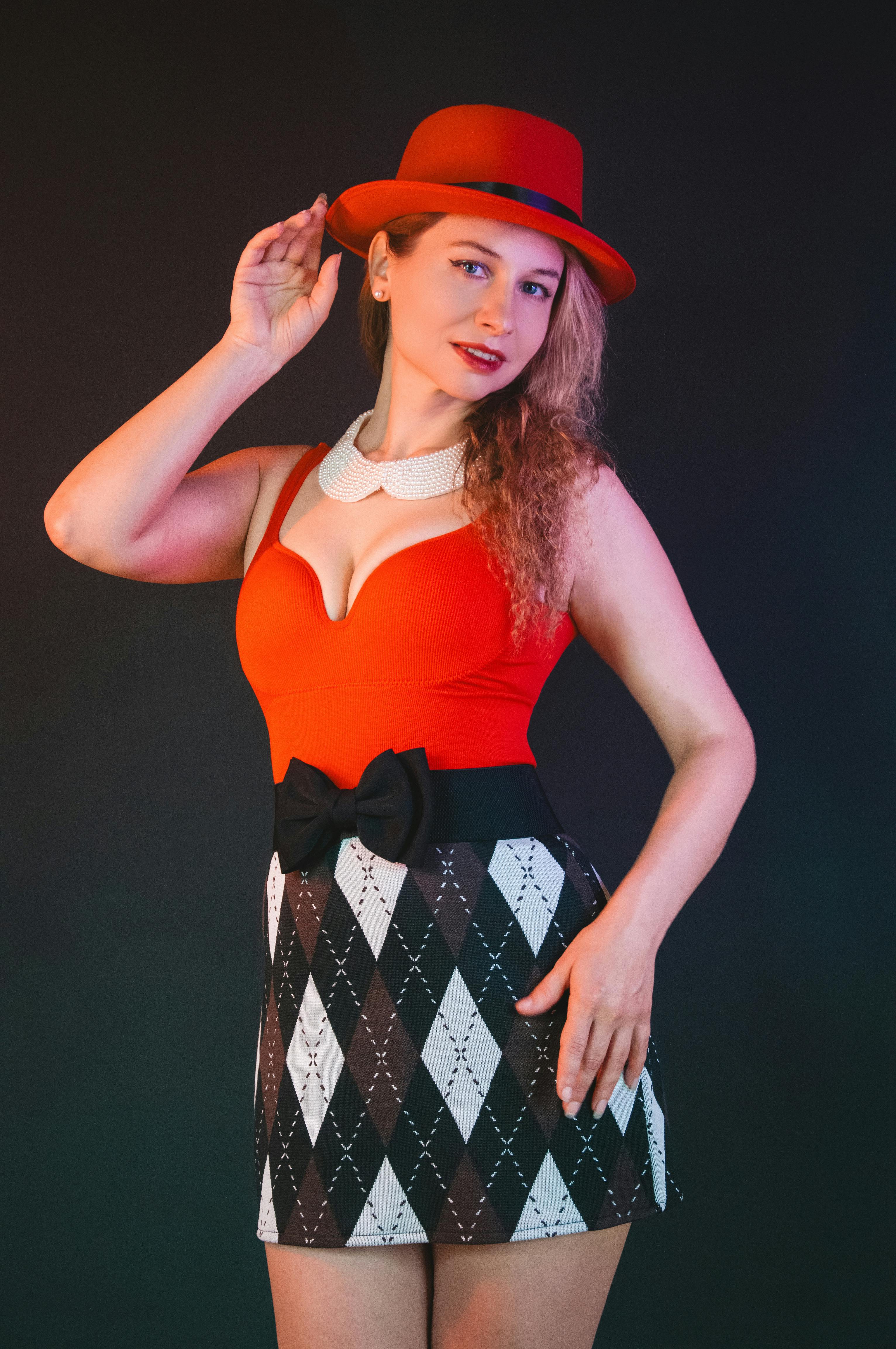 gratis Vrouw poseert met een opvallende rode hoed en een stijlvolle outfit met een rok met ruitpatroon. Stockfoto