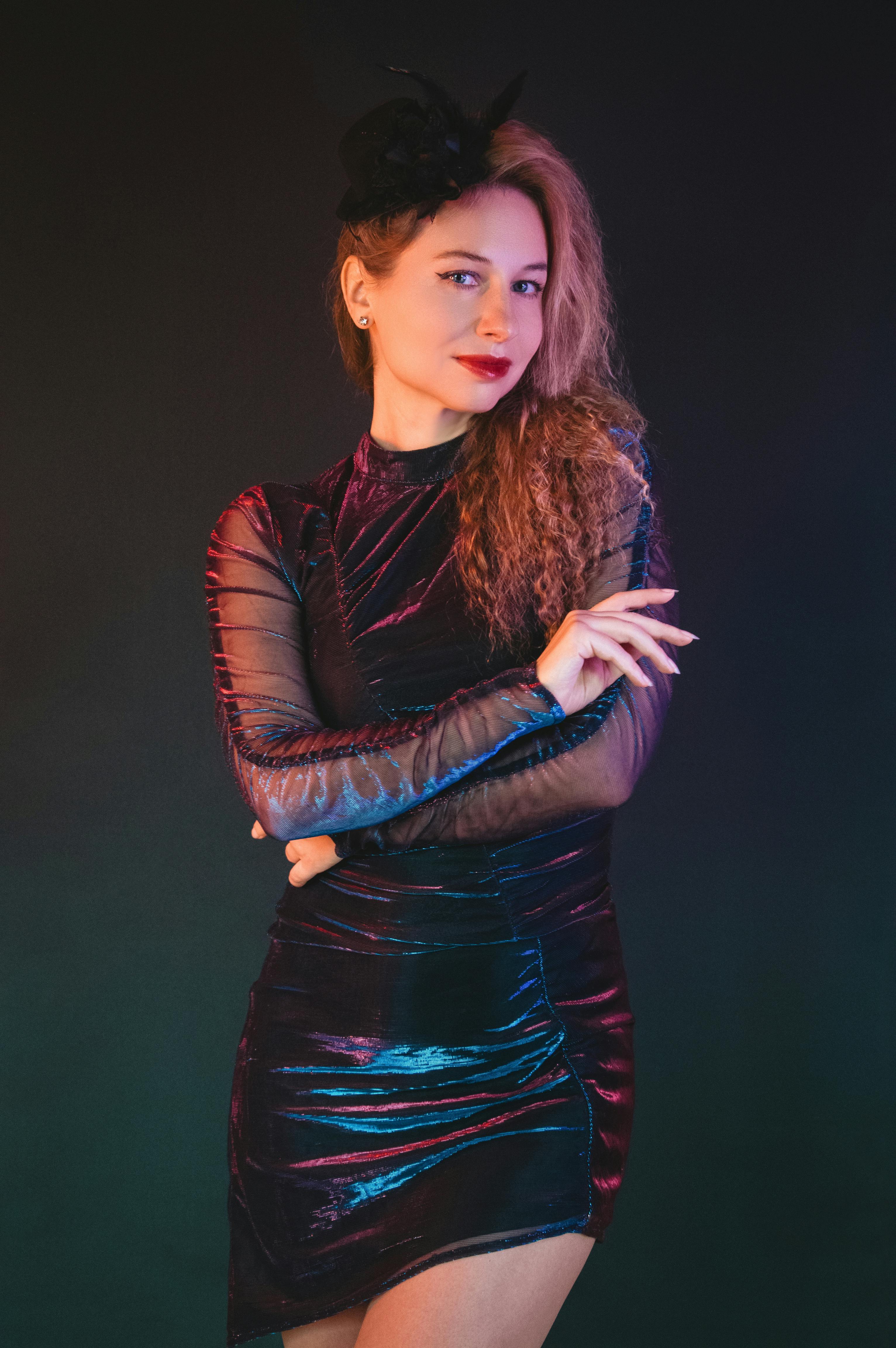 Gratuit O femeie elegantă, într-o rochie neagră stilată, pozează pe un fundal întunecat, cu iluminare vibrantă. Fotografie de stoc